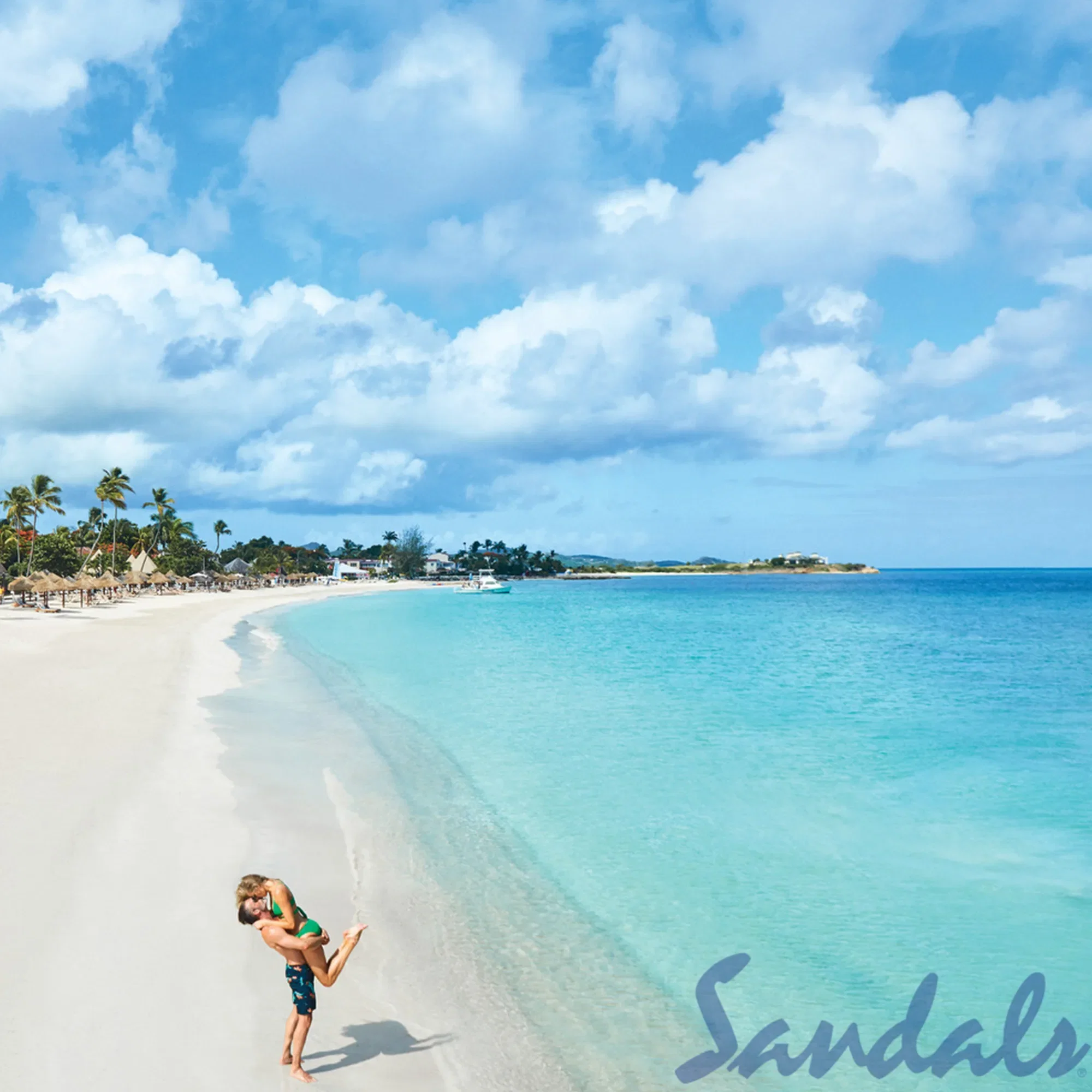 Ein weiter Sandstrand mit klarem, türkisfarbenem Meer, an dem ein Paar fröhlich miteinander spielt. Der Mann hebt die Frau hoch, während sie die warme Strandatmosphäre genießen. Der Himmel ist leicht bewölkt, und am Horizont sind Strandhütten und Palmen zu sehen.