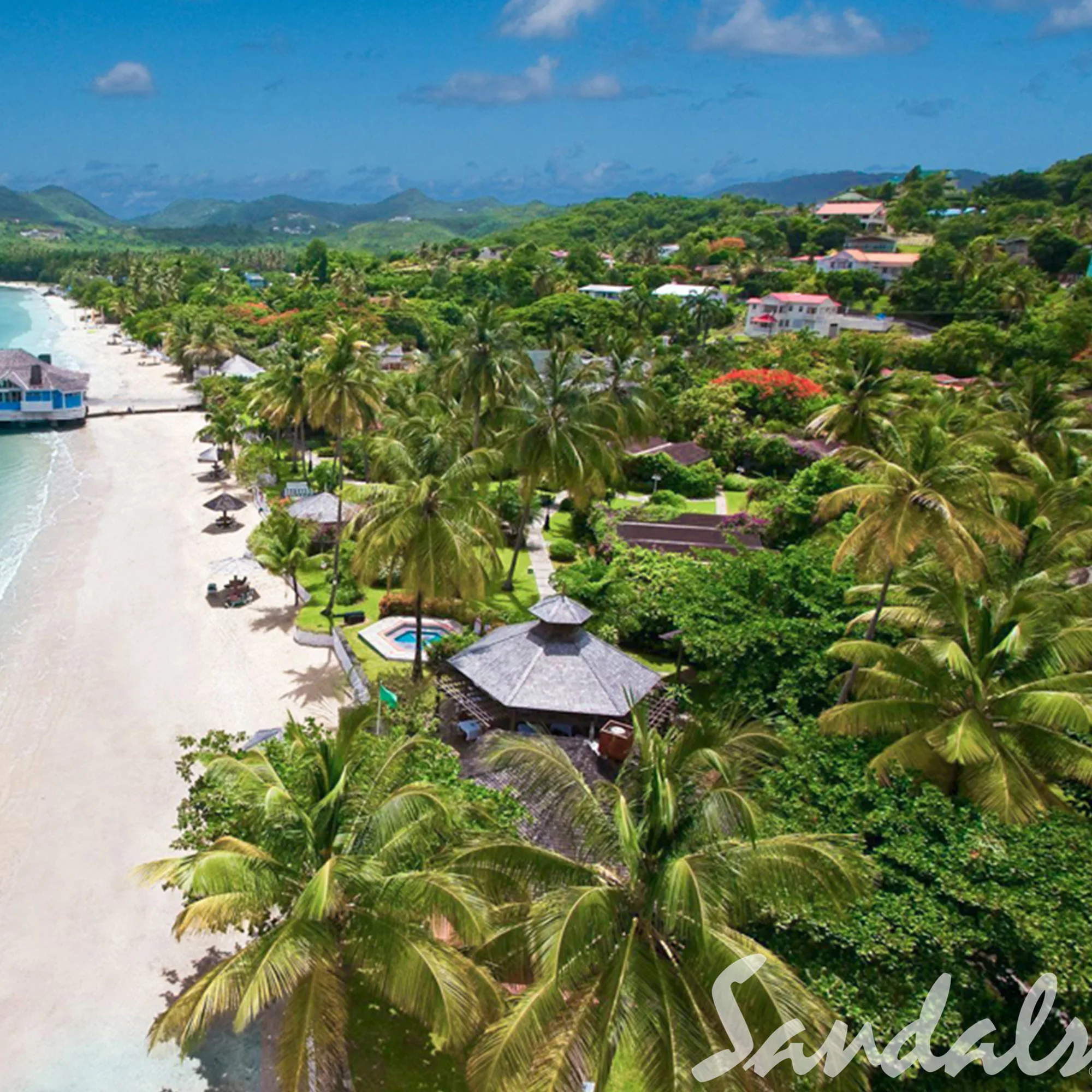 Eine atemberaubende Vogelperspektive auf St. Lucia zeigt Palmen, Strandhütten und üppige tropische Vegetation, die sich bis zum weißen Sandstrand erstrecken. Das klare, blaue Meer glitzert unter dem sonnigen Himmel.