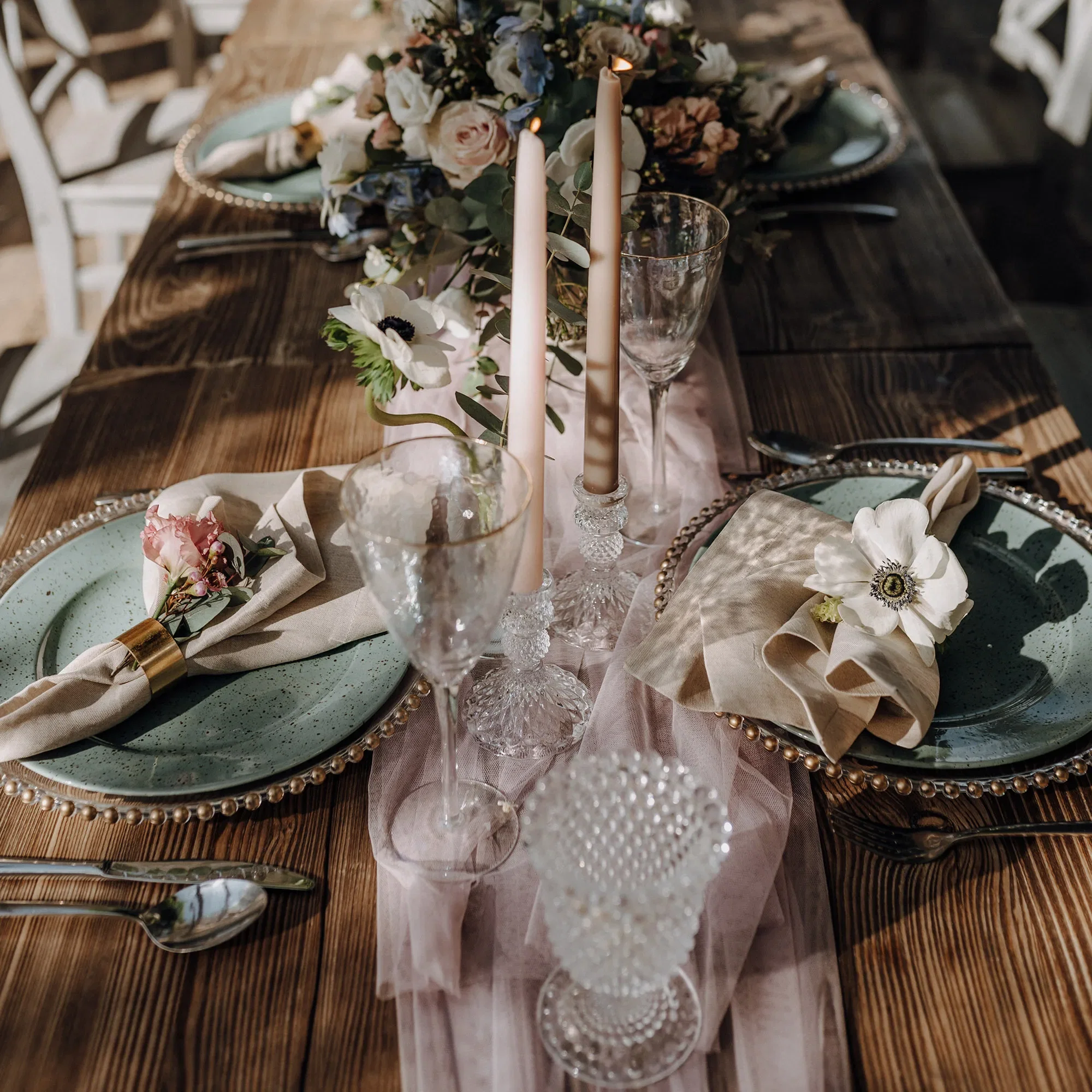 Hochzeitstafel mit Blumenarrangements, Kristallkerzenhaltern und pastellfarbenen Tellern, dekoriert mit Stoffservietten und Anemonenblüten.