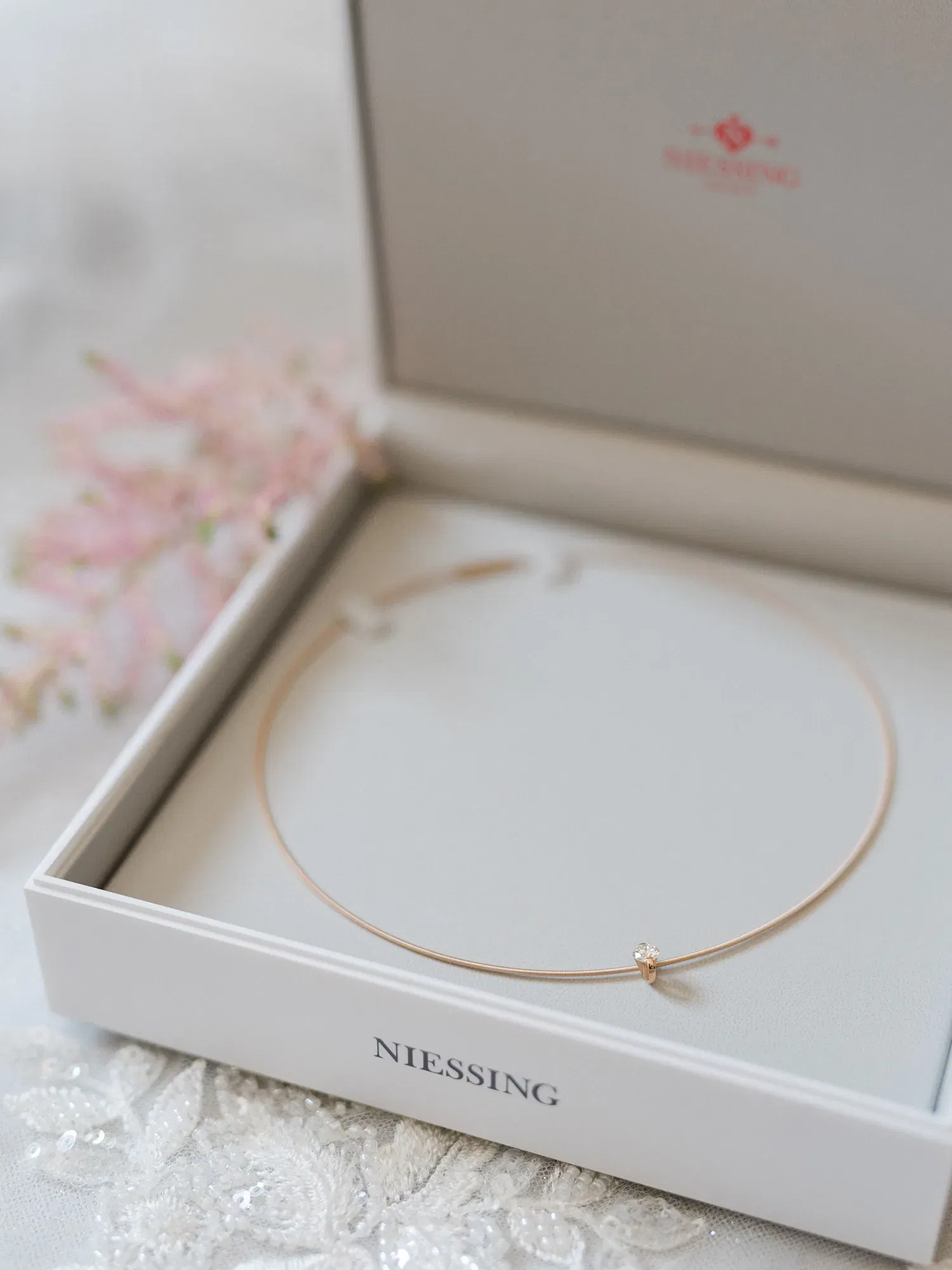 Minimalistische Halskette mit einem einzelnen Diamanten in einer offenen Geschenkbox der Marke Niessing. Die Szene wirkt elegant und unterstreicht den hochwertigen Schmuck.