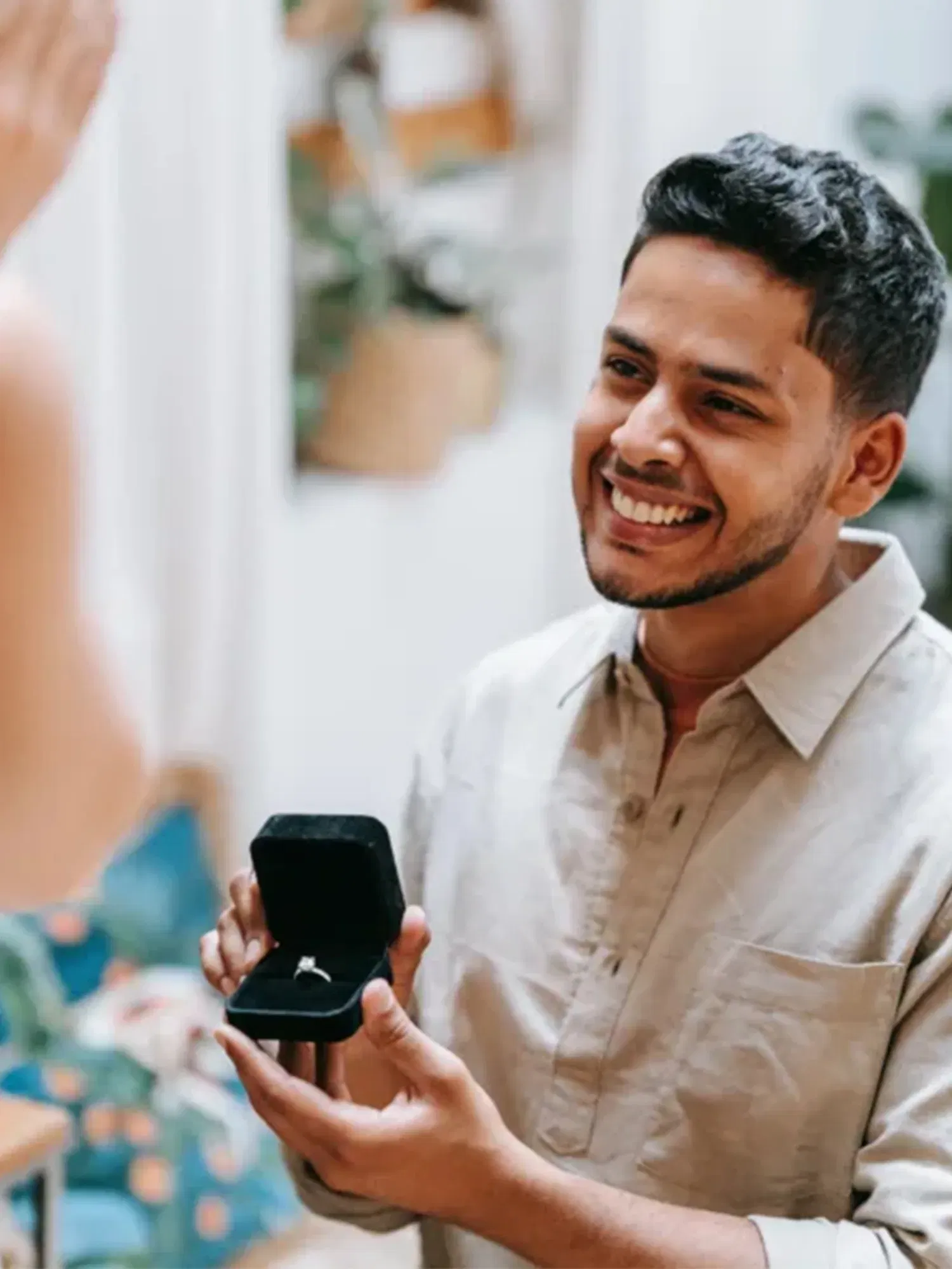 Ein glücklicher Mann hält eine Ringschachtel in der Hand und macht seiner Partnerin einen Heiratsantrag.