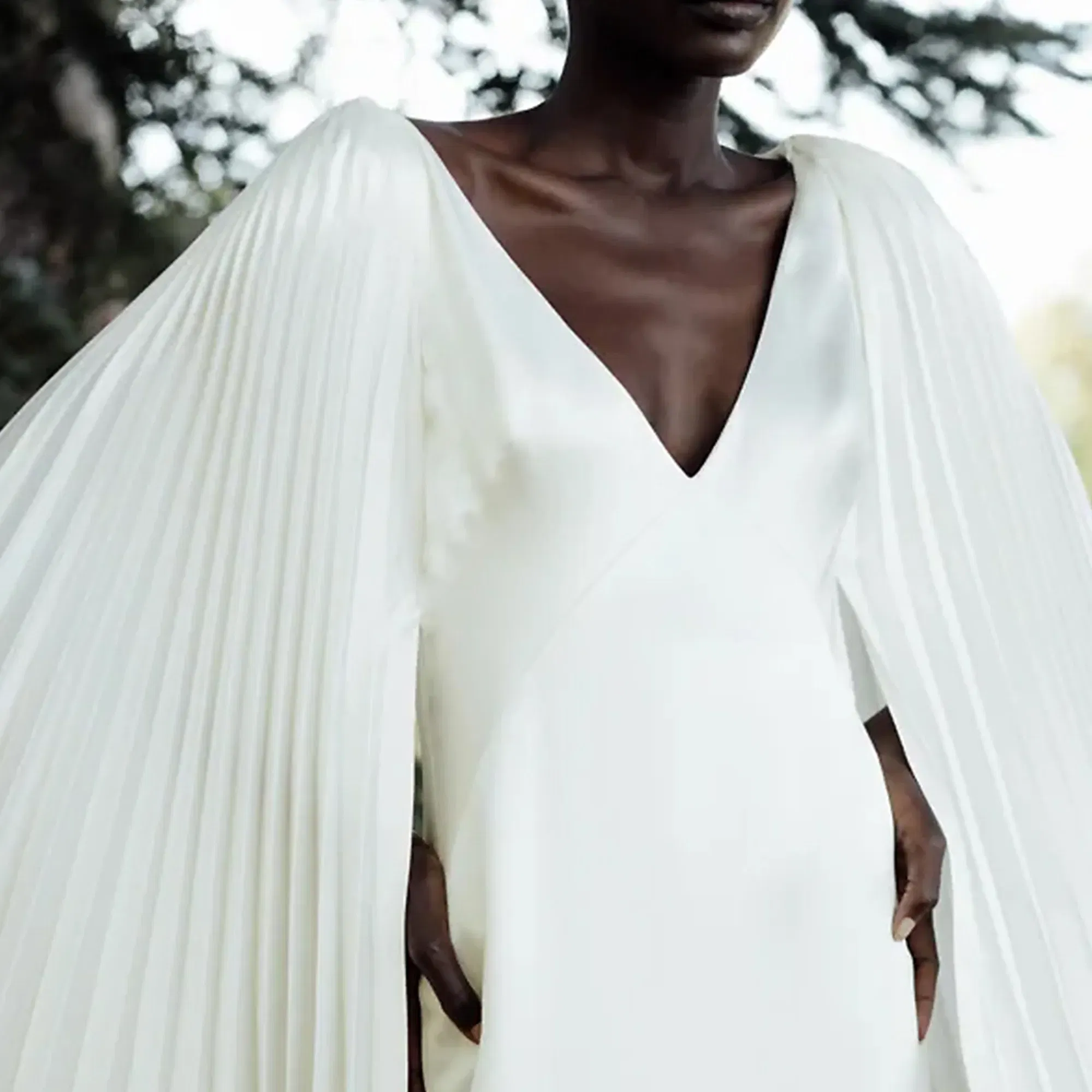 Detailaufnahme eines modernen Hochzeitskleides mit dramatischen, weiten Ärmeln, die in Falten gelegt sind, und einem tiefen Ausschnitt. Der minimalistische Stil betont die schlichte Eleganz des Kleides.