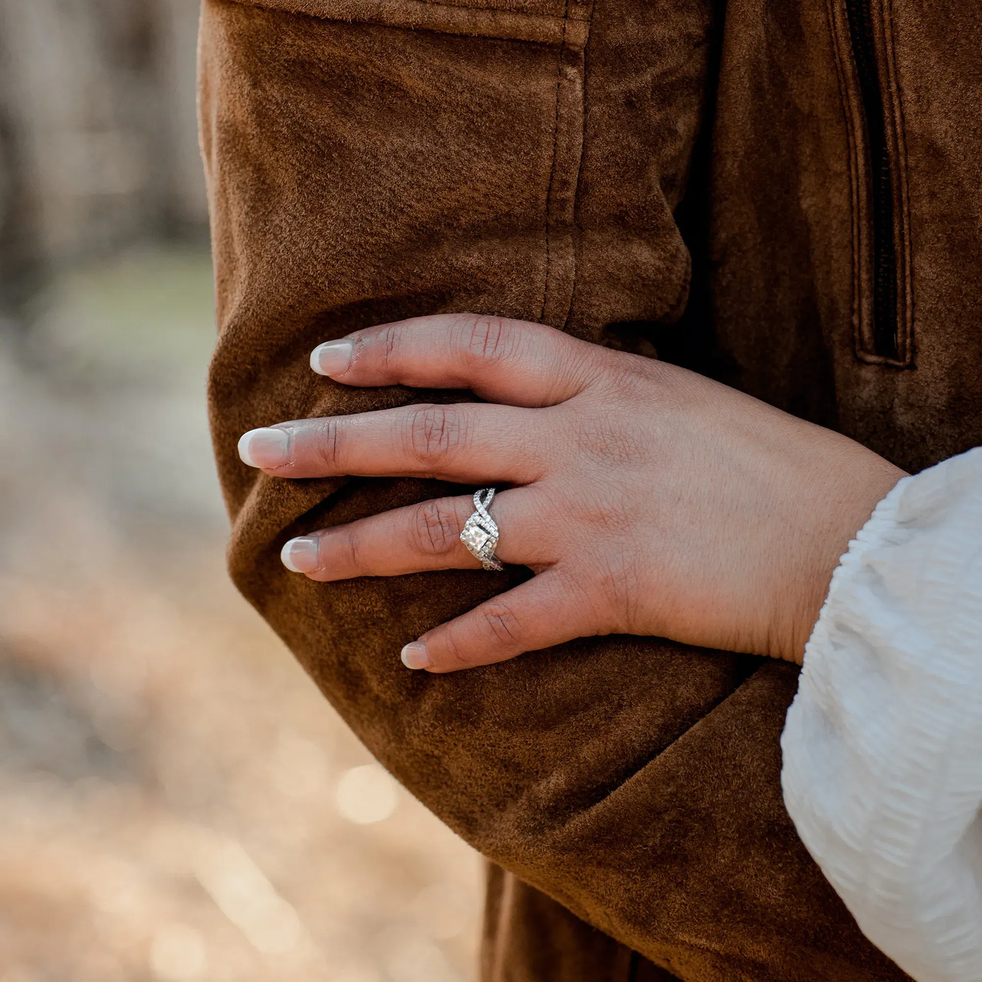 Eine Hand mit einem Verlobungsring ruht sanft auf dem Ärmel eines Partners in dieser symbolträchtigen Verlobungsszene.