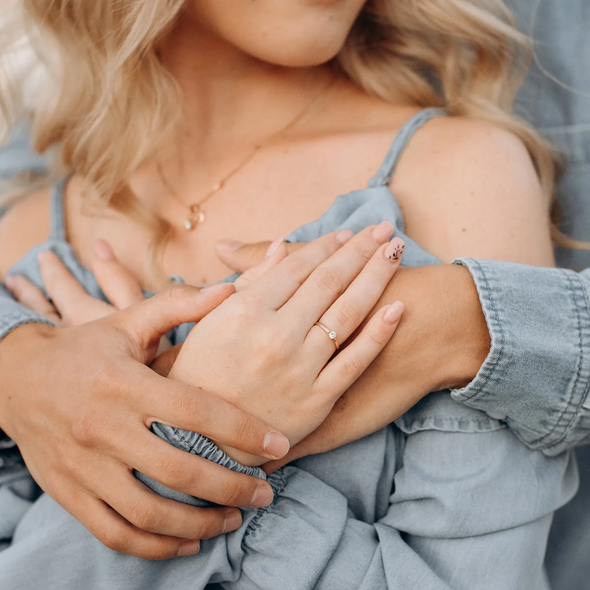 Ein romantischer Moment, in dem eine Frau ihren Verlobungsring zeigt, während ihr Partner sie von hinten sanft umarmt.