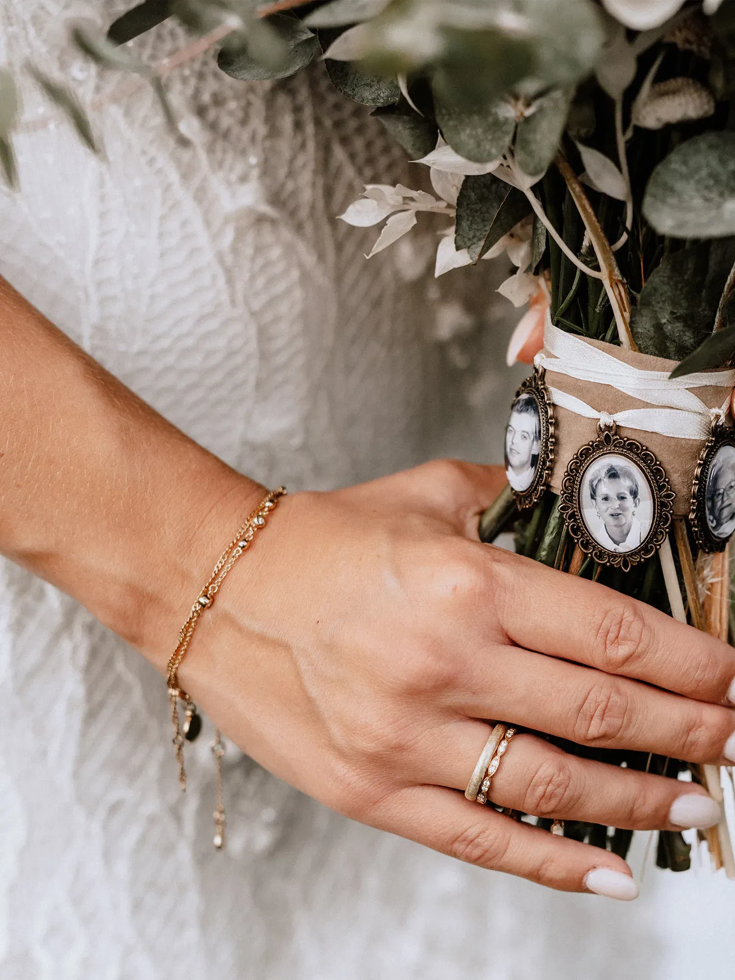 Detailaufnahme einer Brauthand, die einen Strauß mit persönlichen Fotos in Vintage-Medaillons umschlingt. Die Braut trägt ein schlichtes goldenes Armband und zwei goldene Ringe.