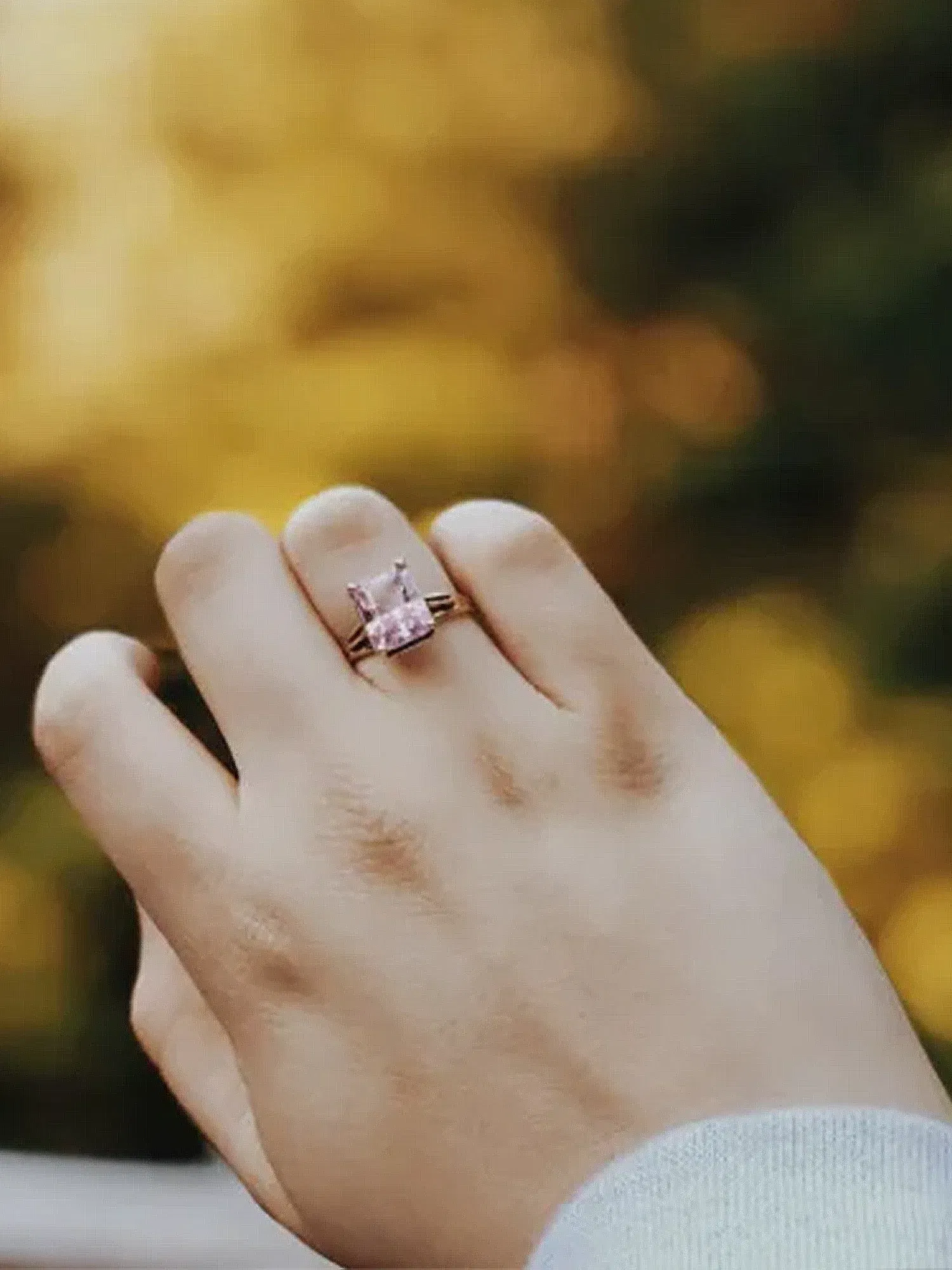 Ein Verlobungsring mit einem auffälligen, farbigen Stein wird in einer herbstlichen Kulisse zur Schau gestellt.