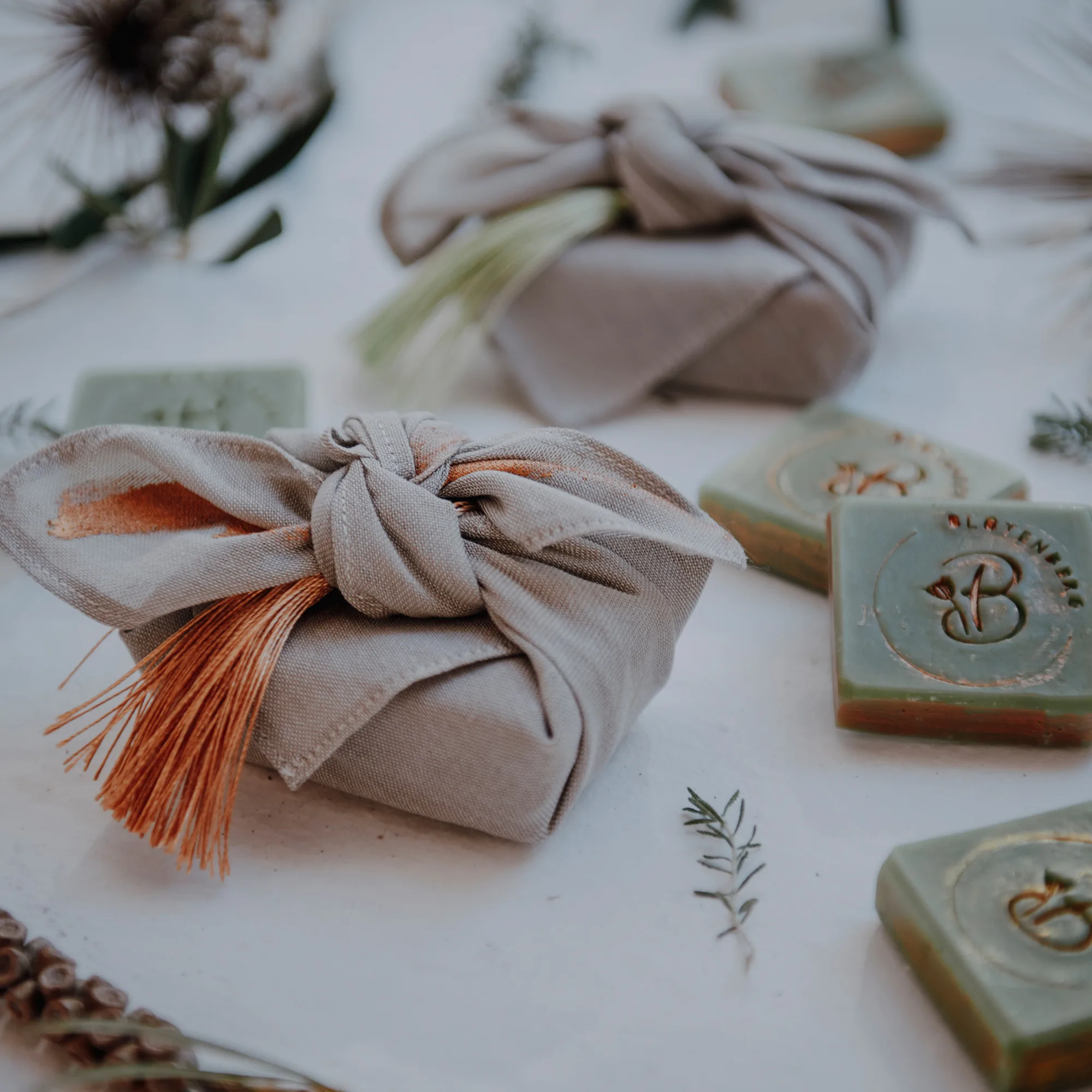 Nahaufnahme von nachhaltigen Hochzeitsgastgeschenken, eingewickelt in Leinenstoff, mit handgemachten Seifen und dekorativen Zweigen.