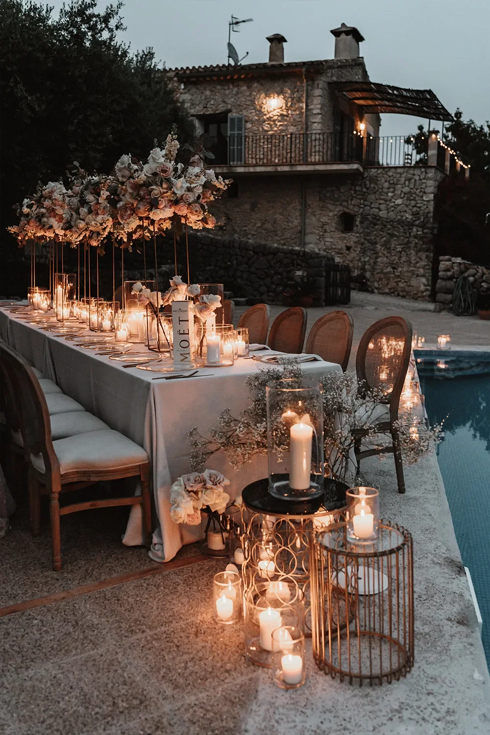 Stimmungsvolle Hochzeits-Tafel bei Dämmerung, umgeben von Kerzenlicht und romantischen Blumenarrangements, mit rustikalem Hintergrund.