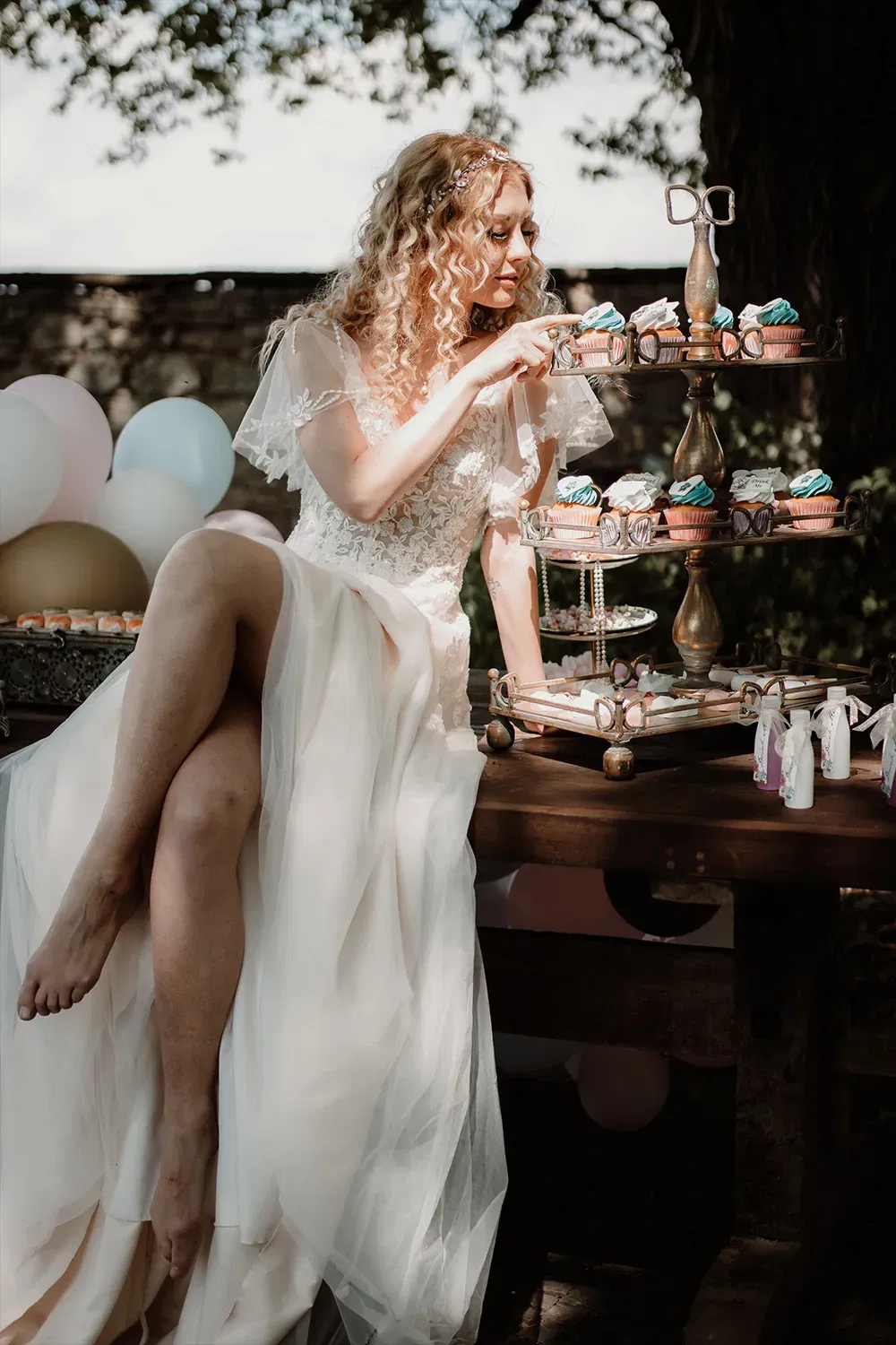 Die Braut in einem eleganten Hochzeitskleid sitzt entspannt neben einem Cupcake-Ständer, umgeben von Ballons und dekorativen Süßigkeiten.