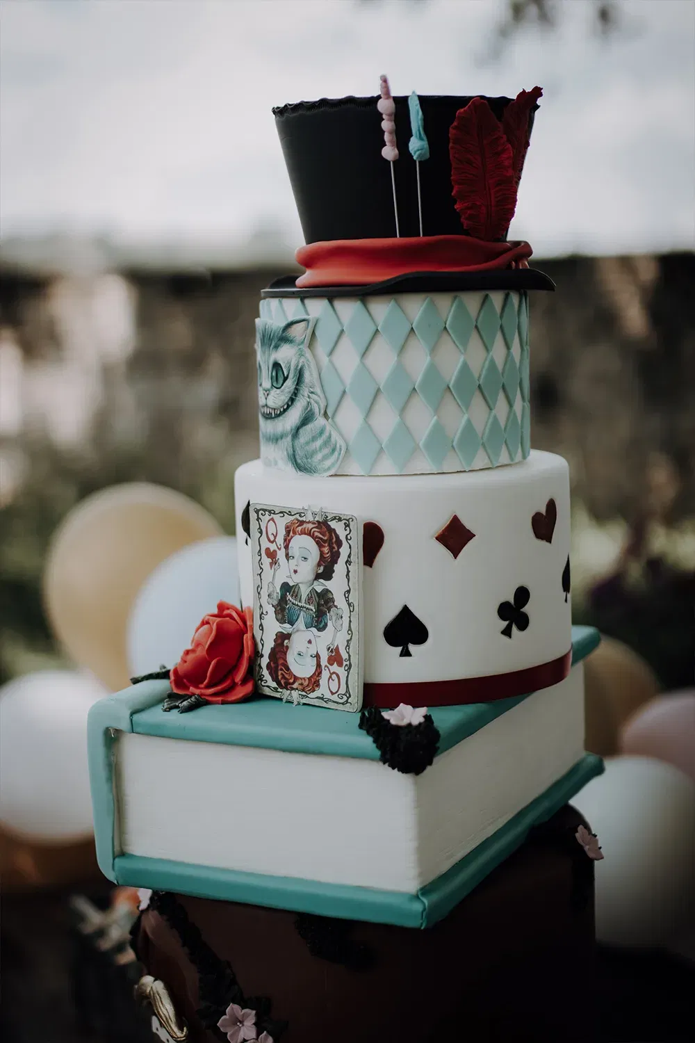 Verspielte Hochzeitstorte inspiriert von "Alice im Wunderland" mit Details wie einem Zylinderhut, der Grinsekatze und Spielkarten.