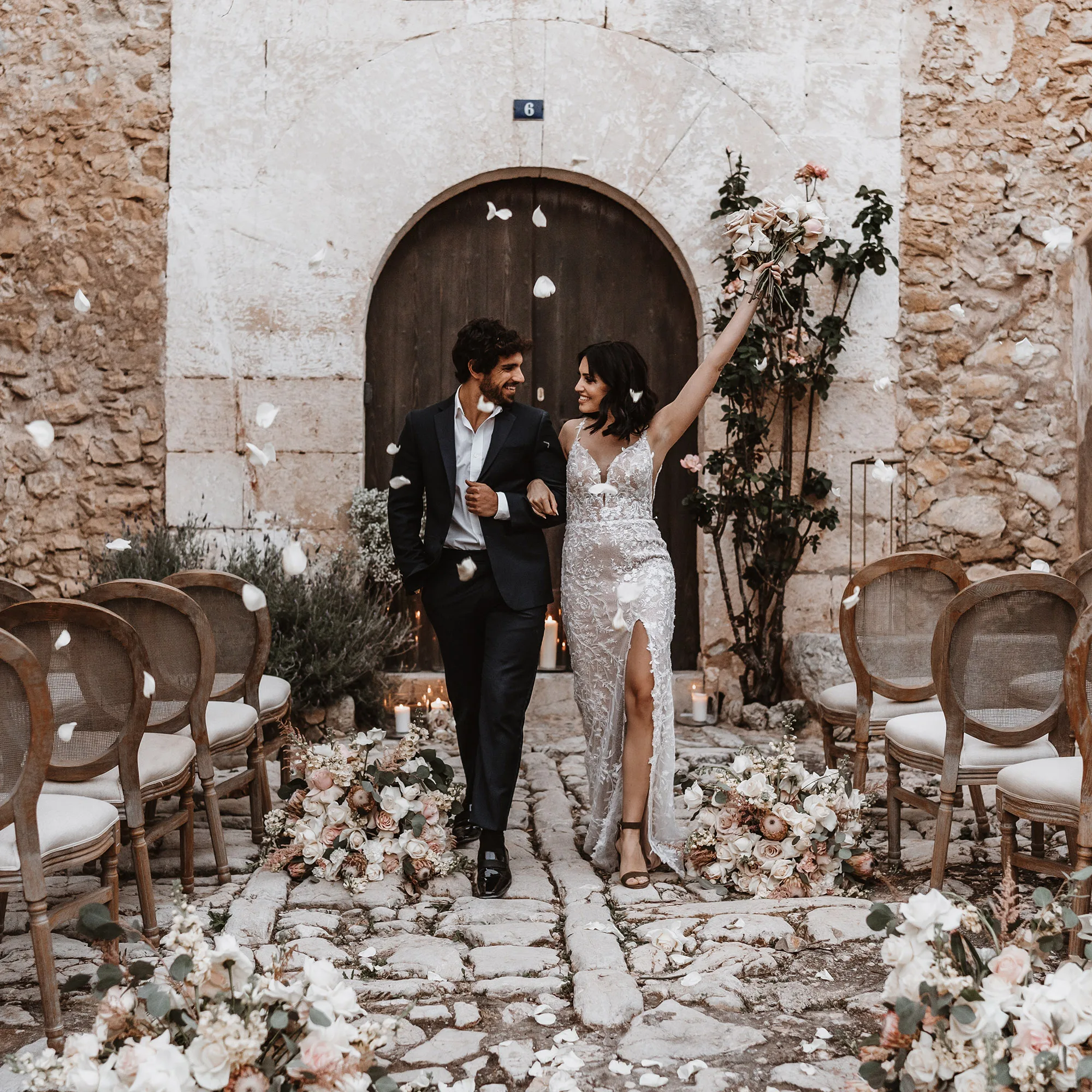 Nach der Trauung schreitet das Brautpaar glücklich durch einen Gang mit Blumenarrangements, während weiße Blütenblätter um sie herum schweben.