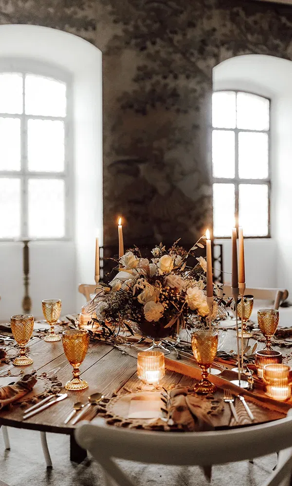 Die Hochzeitstafel ist elegant dekoriert mit Blumen, goldfarbenen Trinkgläsern und flackernden Kerzen auf einem Holztisch.