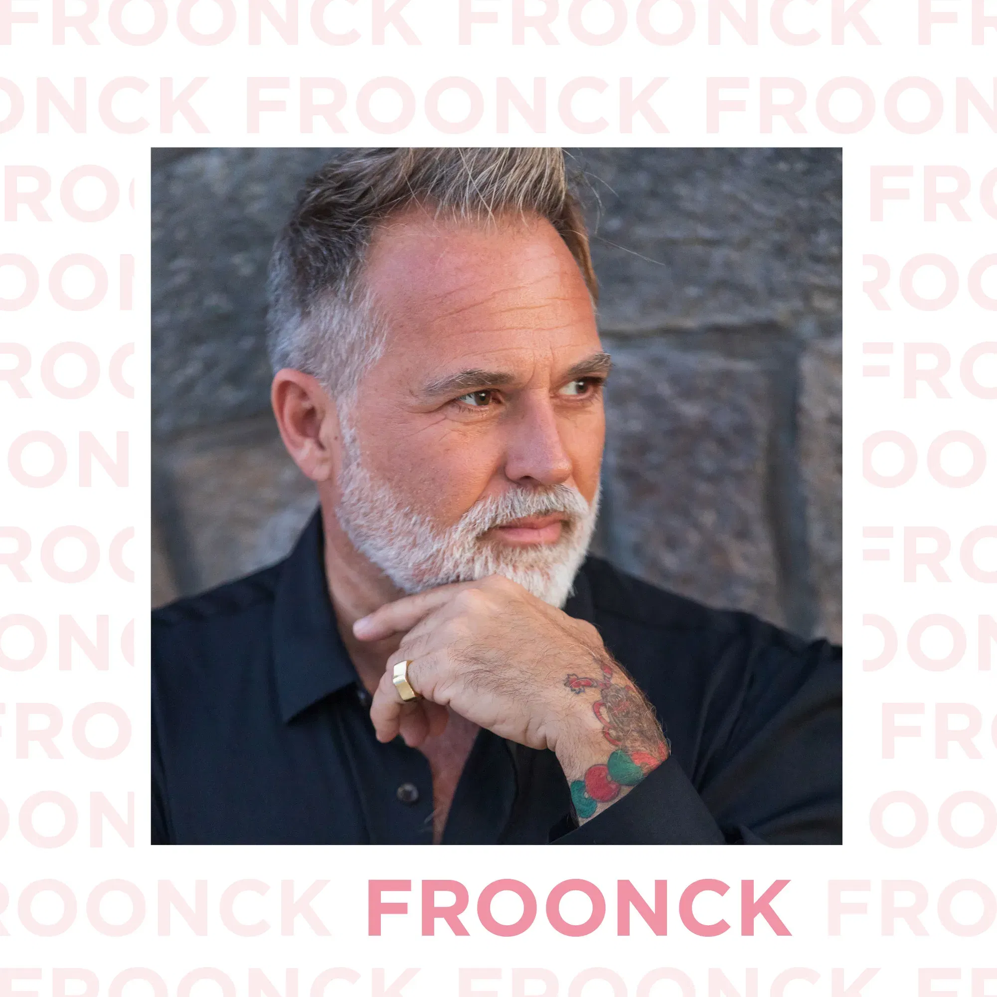 Froonck, Hochzeitsplaner, in einem nachdenklichen Moment, mit der Hand am Kinn, vor einer grauen Steinmauer posierend.