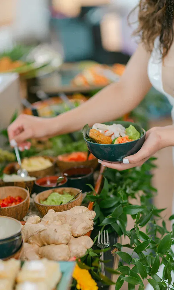 Ein reich gedecktes Buffet, das gesunde und köstliche Gerichte präsentiert. Die Speisen sind auf Blättern angerichtet, darunter frische Kräuter und Gemüse, und verschiedene Dips und Gewürze in Schalen.