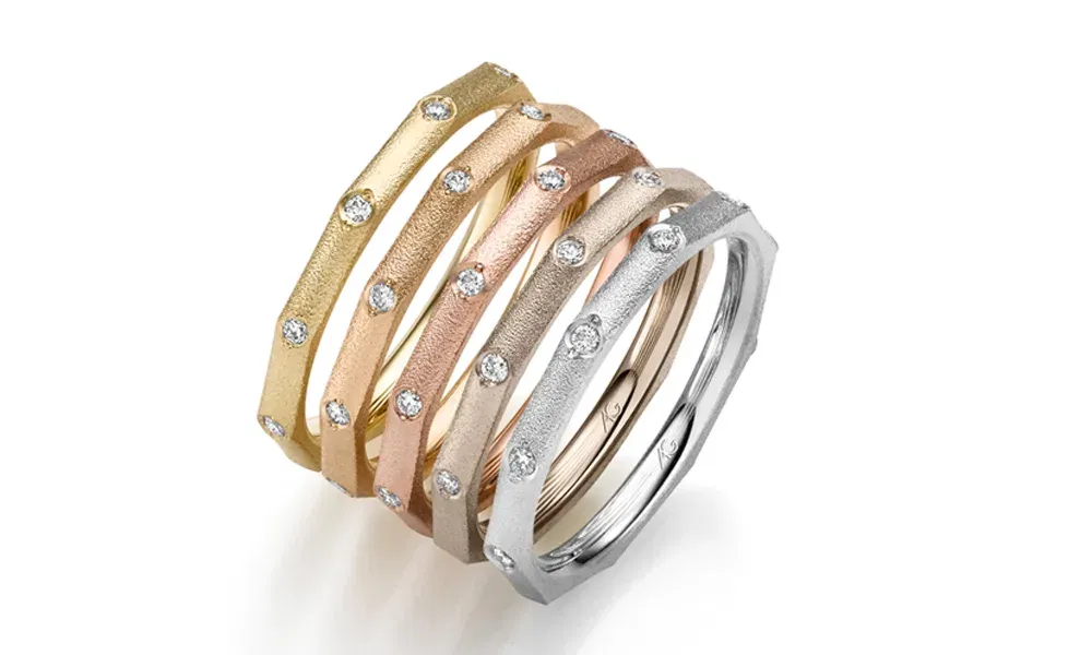 Fünf schmale Ringe in Gelb-, Rosé- und Weißgold, die übereinander gestapelt sind. Jeder Ring ist mit funkelnden Diamanten besetzt, die in gleichmäßigen Abständen auf der facettierten Oberfläche platziert sind. Das Set besticht durch sein edles und modernes Design.