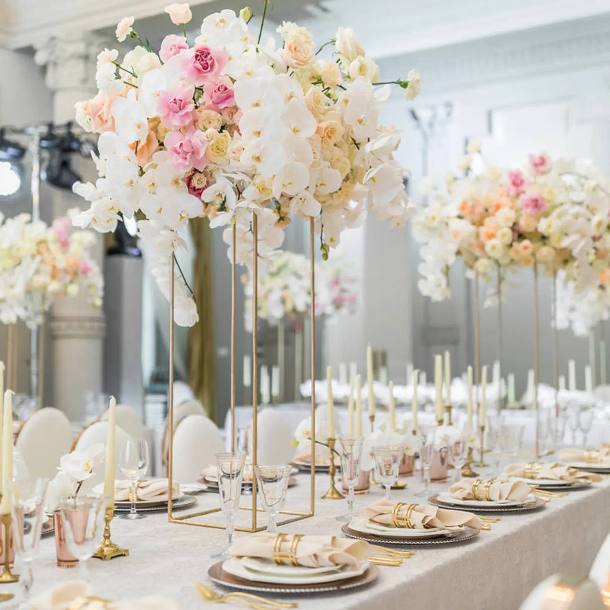 Elegant eingedeckter Hochzeitstisch mit üppigen Blumengestecken in Rosa, Weiß und Creme. Goldene Kerzenhalter und gläserne Weingläser unterstreichen die luxuriöse Tischdekoration.