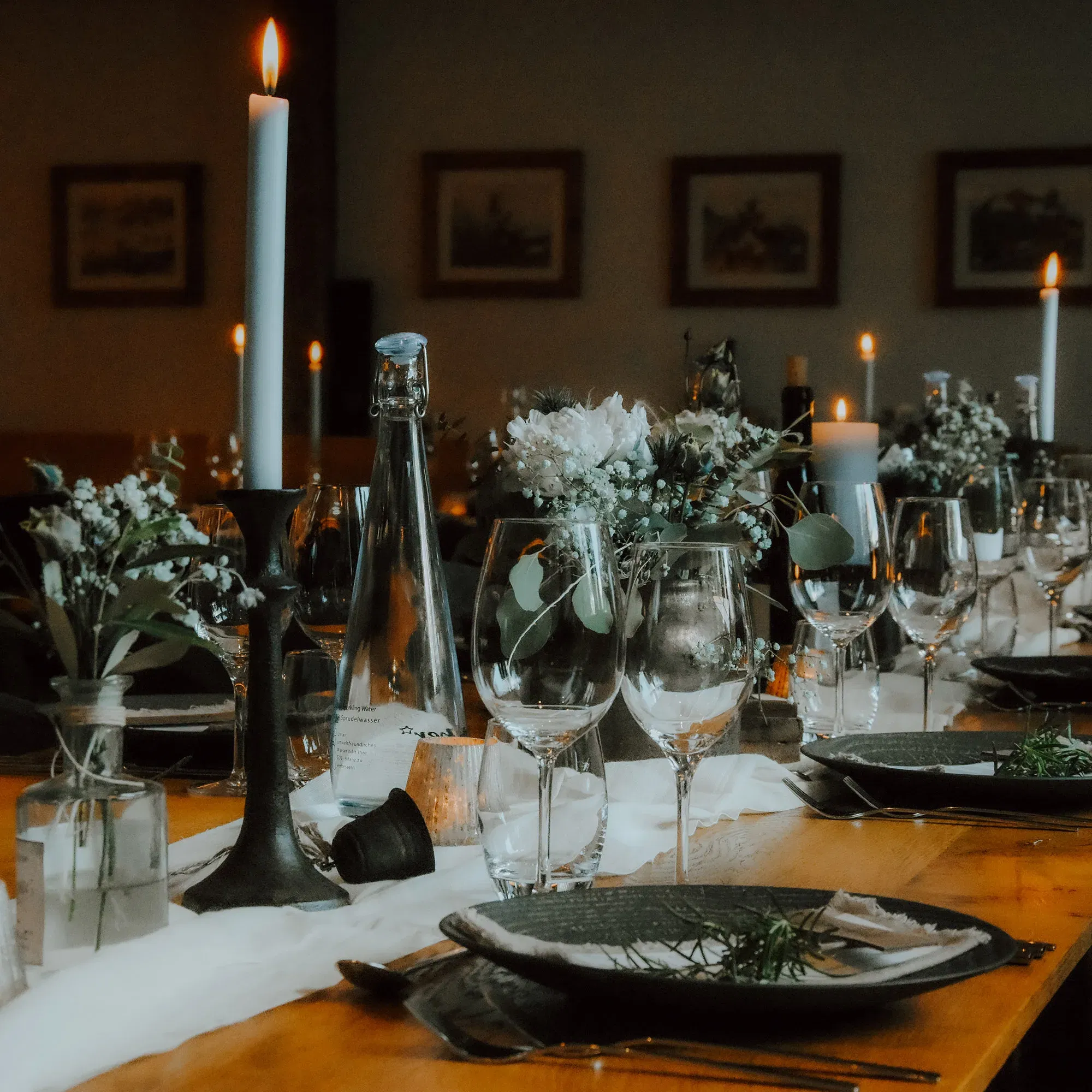 Eine lange Hochzeitstafel, dekoriert mit Blumen, Weingläsern und hohen weißen Kerzen, die ein gemütliches Ambiente im Kerzenschein schafft.