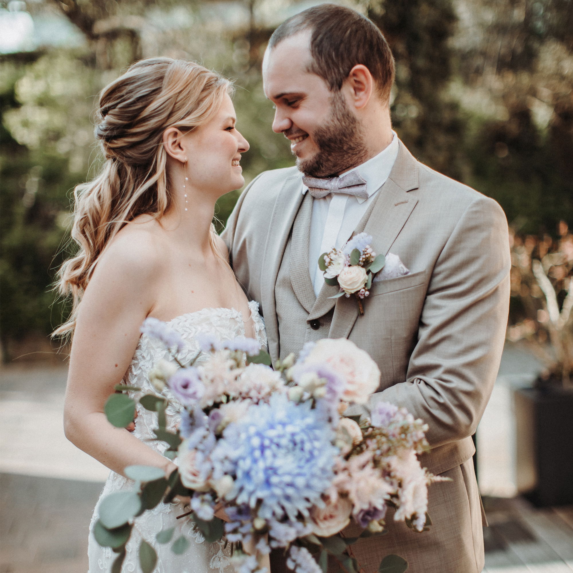 Das Brautpaar schaut sich während eines intimen Moments nach der Zeremonie in die Augen. Die Braut hält einen wunderschönen Blumenstrauß, und der Bräutigam trägt einen eleganten hellen Anzug.