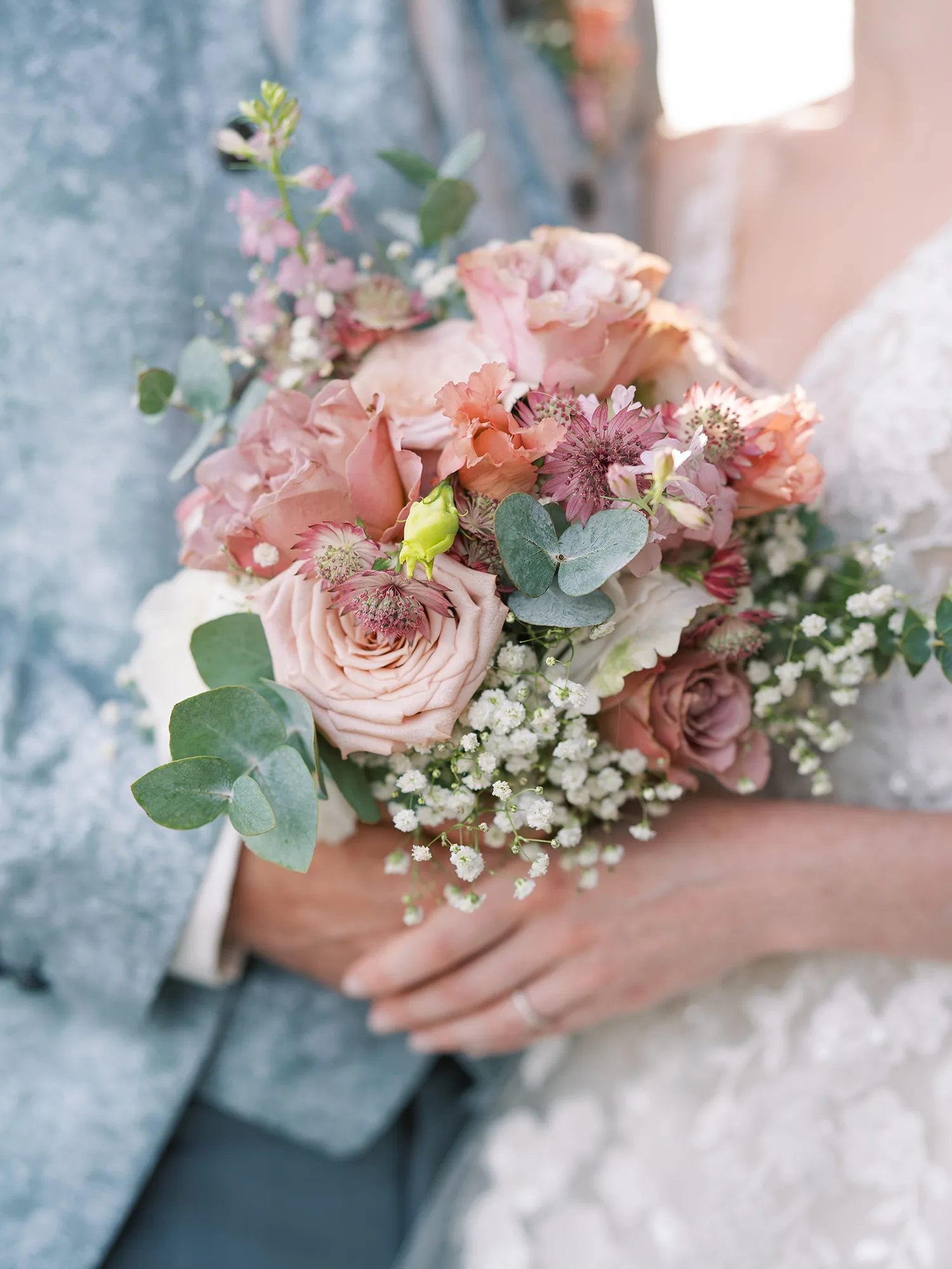 Blumiger Brautstrauß in Pastelltönen, mit Rosen, Eukalyptus und Schleierkraut, in den Händen eines frisch verheirateten Paares.