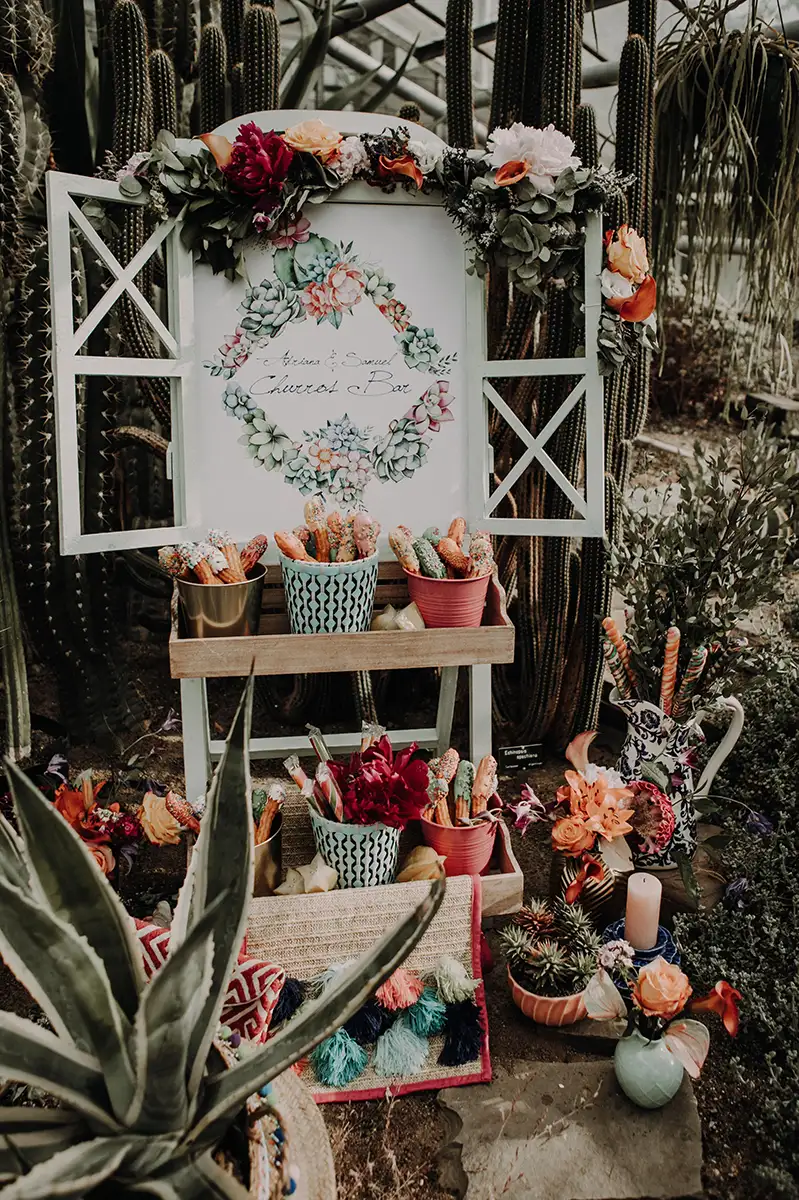 Ein Hochzeits-Churros-Buffet, verziert mit bunten Blumentöpfen und Sukkulenten, bietet eine farbenfrohe und lebendige Kulisse für die Gäste.