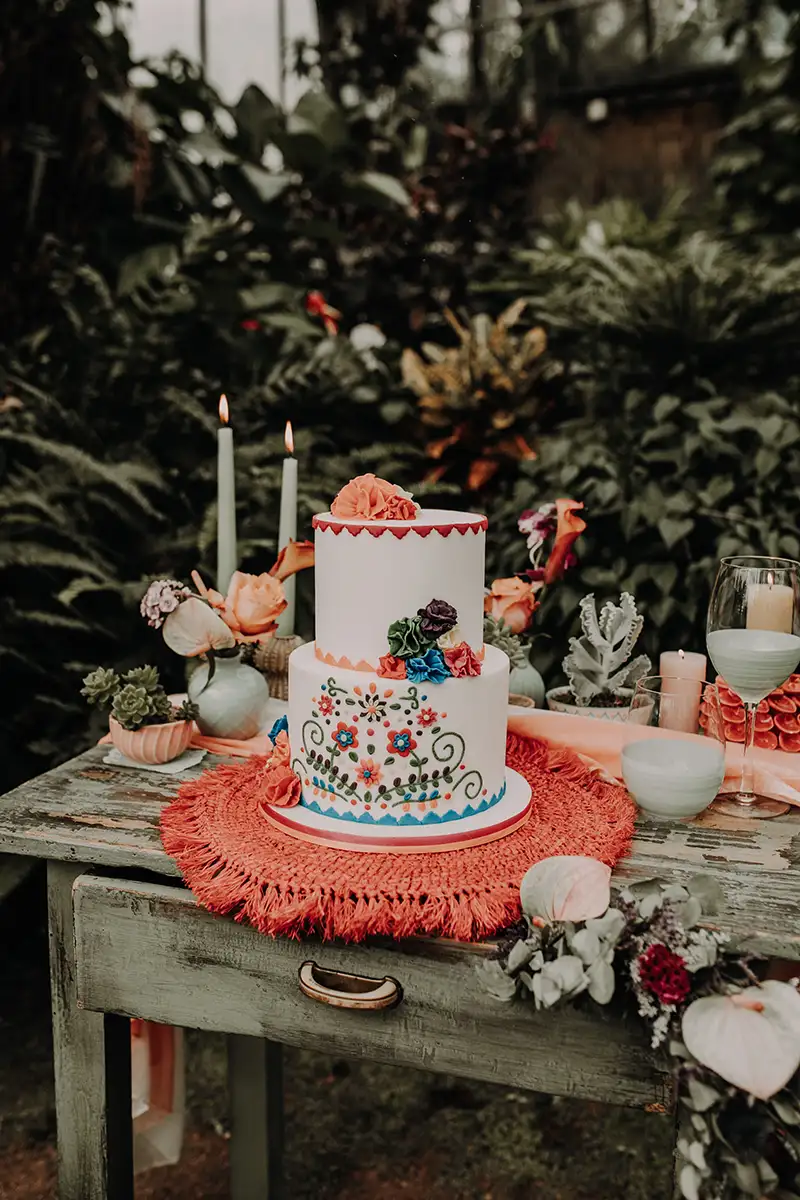 Eine dekorierte Hochzeitstorte mit floralen Verzierungen, arrangiert auf einem Holztisch mit Kerzen und weiteren Blumenakzenten.