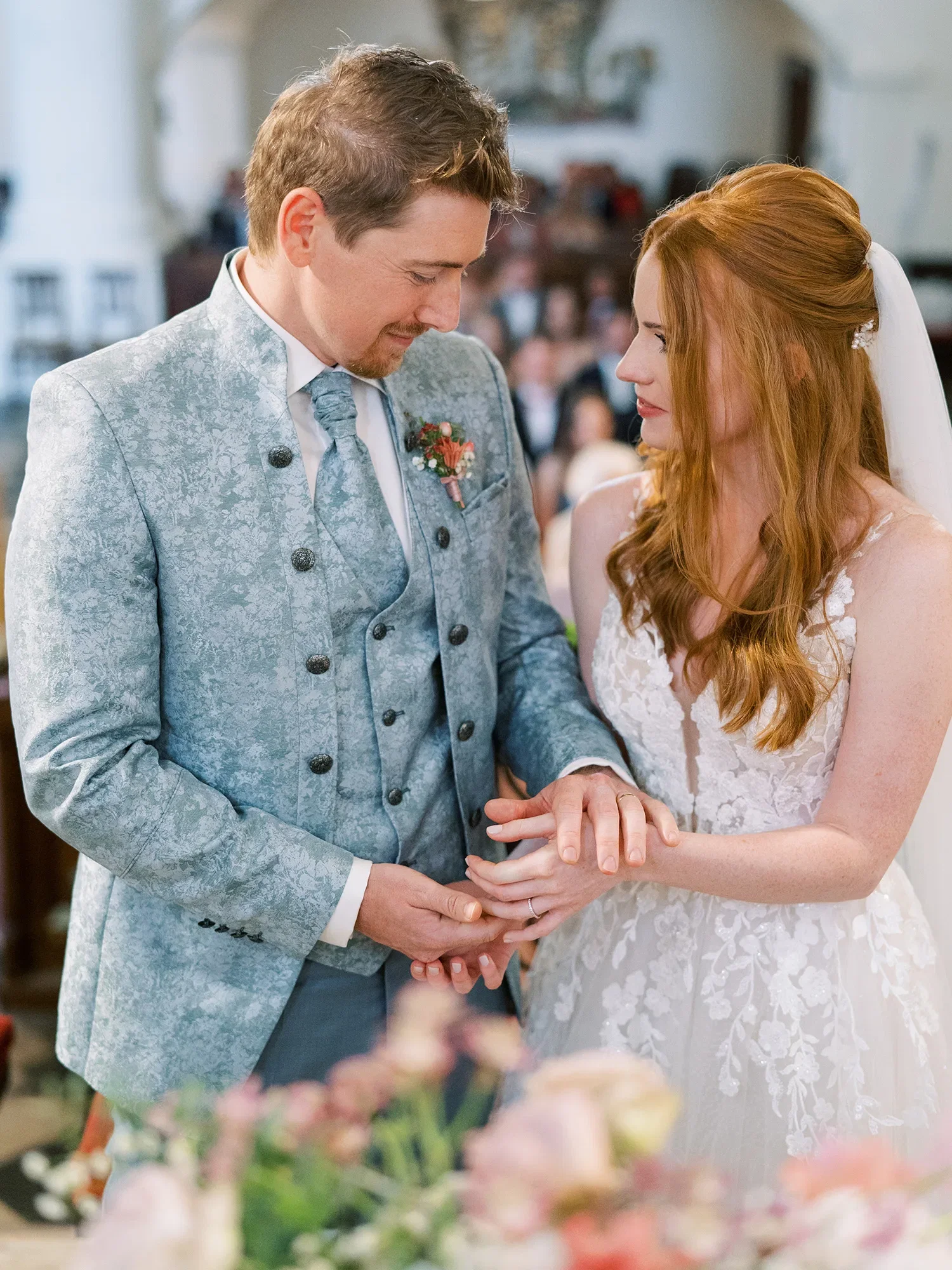 Emotionale Trauung, bei der der Bräutigam der Braut den Ring auf den Finger steckt, beide tragen elegante Hochzeitskleidung.