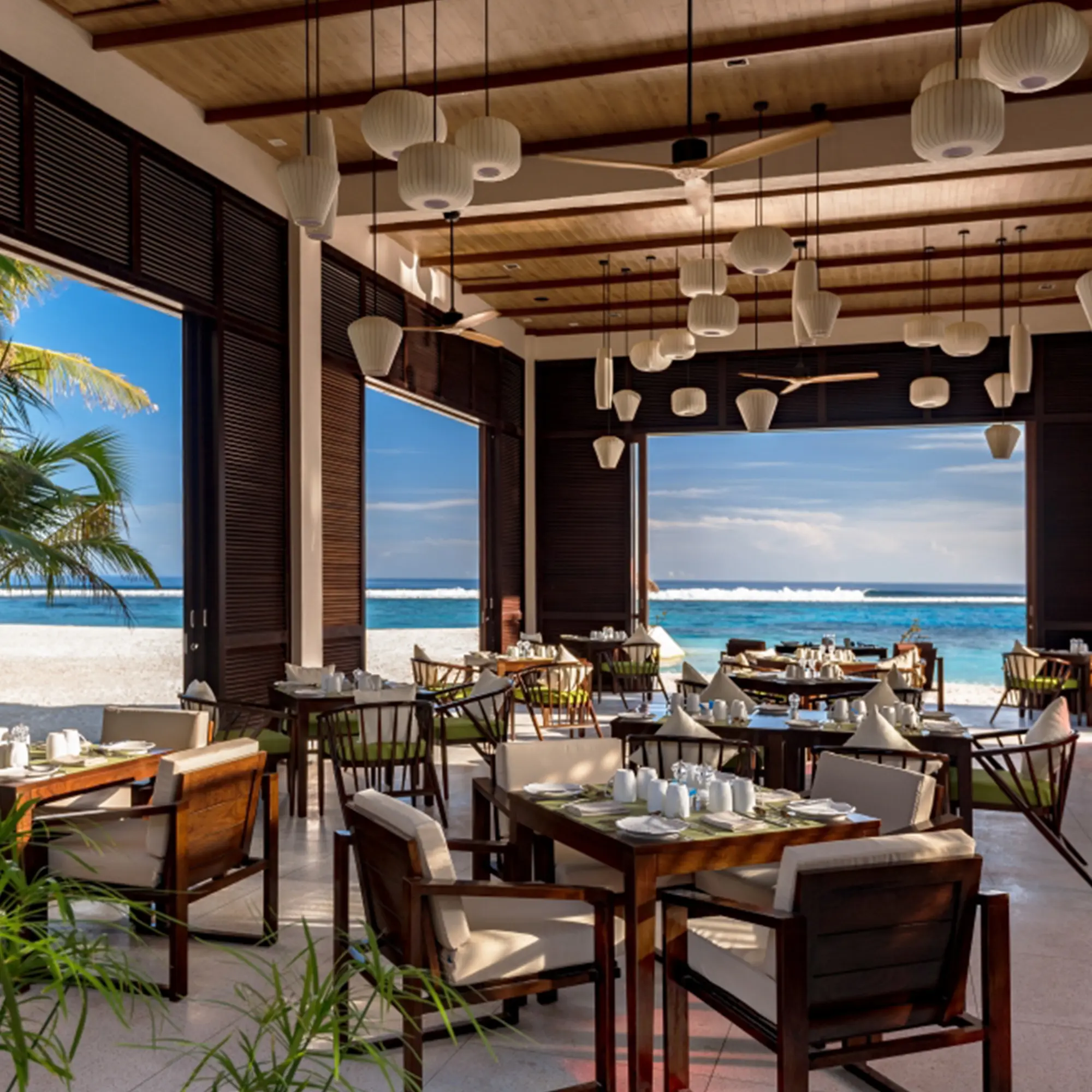 Strandrestaurant mit offener Architektur, modernem Holzmobiliar und einem atemberaubenden Blick auf das Meer, serviert exquisite Küche in einem entspannten Ambiente.