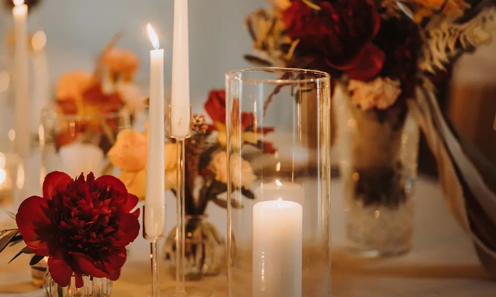 Stimmungsvolle Tischdekoration für eine Hochzeit: Rote Pfingstrosen, Kerzen in hohen Glaszylindern und zarte Blumenarrangements in warmen Farben sorgen für eine romantische Atmosphäre auf der Festtafel.