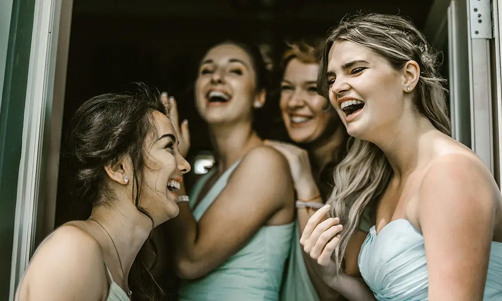 Fröhliche Brautjungfern in mintfarbenen Kleidern lachen zusammen in einem Türrahmen. Sie genießen den Moment vor der Hochzeit und wirken ausgelassen und glücklich.
