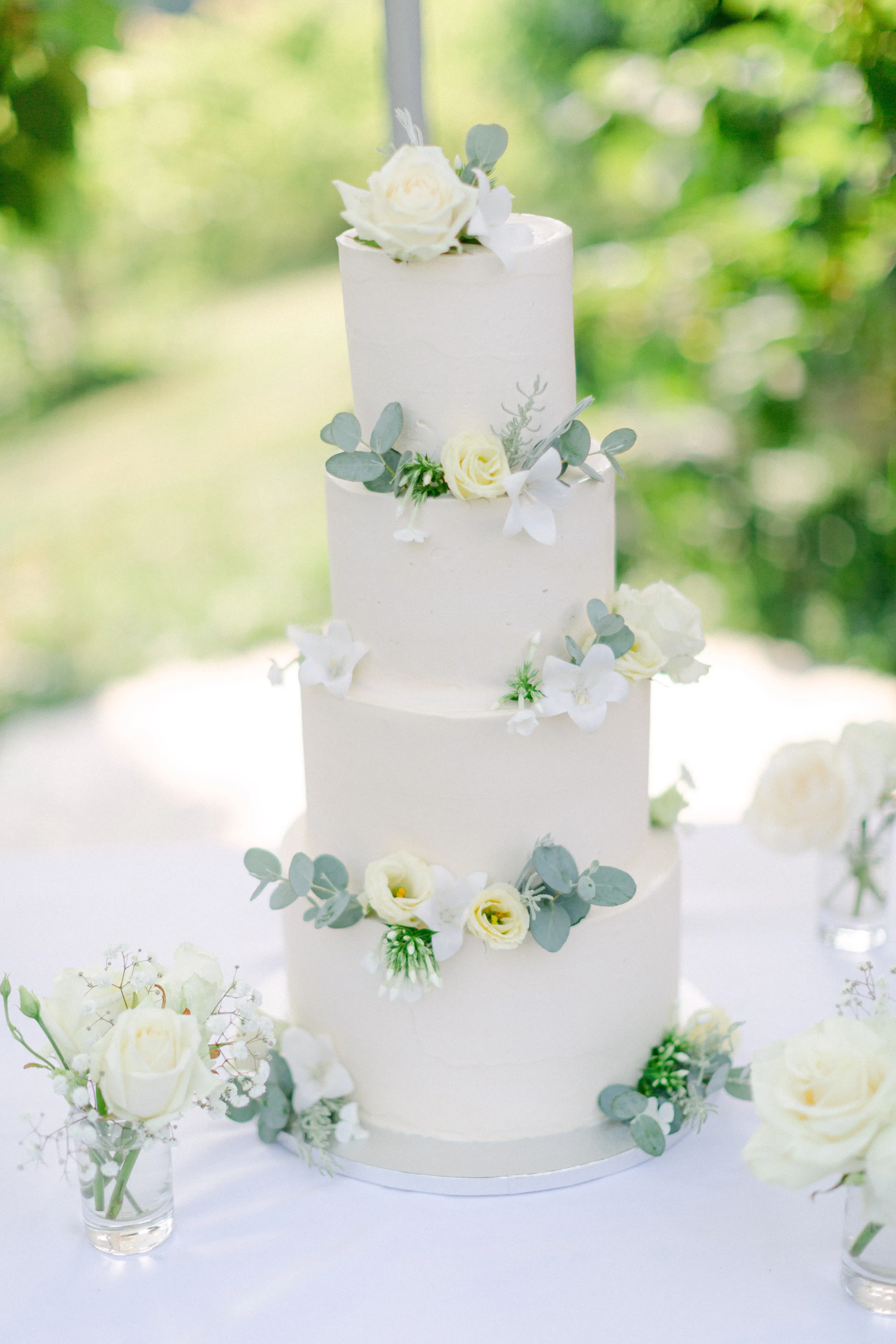 Dreistöckige Hochzeitstorte, verziert mit weißen Rosen und Eukalyptusblättern, steht auf einem Tisch mit natürlicher Blumendeko.