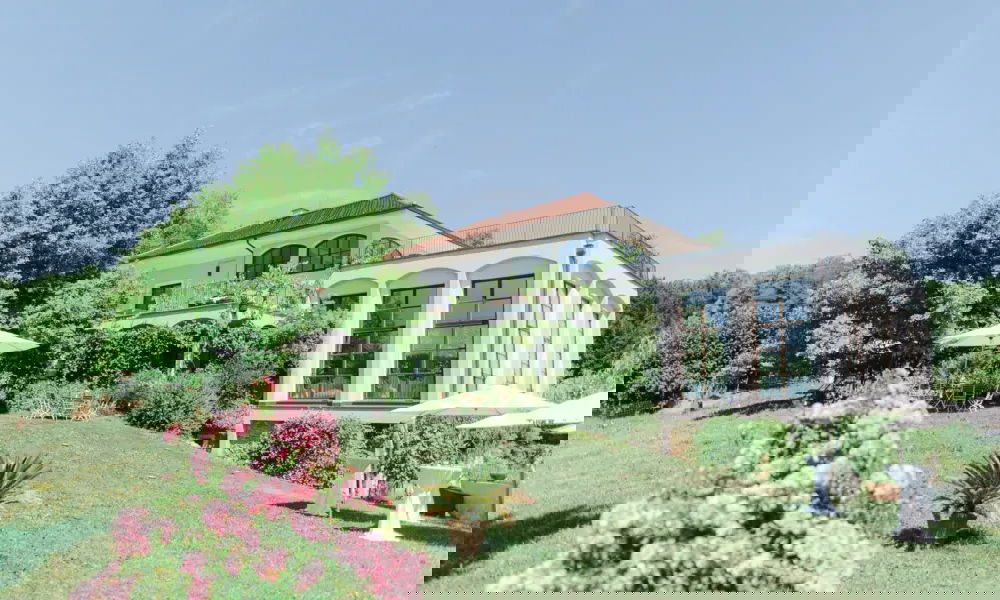 Ein elegantes Gebäude inmitten einer grünen Landschaft, umgeben von Bäumen und blühenden Rosen im Vordergrund.