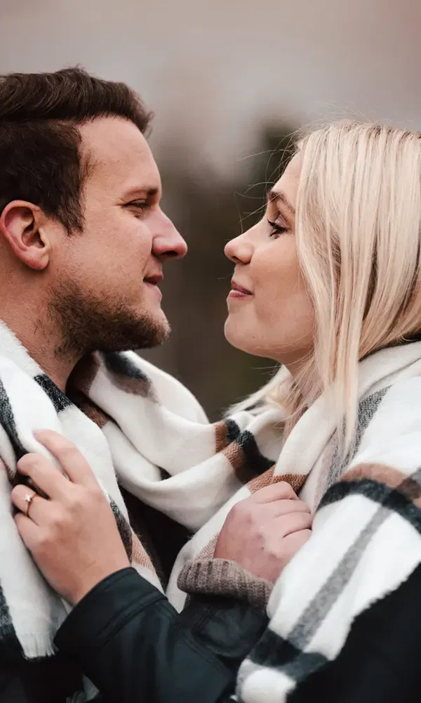 Nahaufnahme eines Paares, das sich in einen warmen Schal kuschelt und sich liebevoll ansieht, bereit für ihr gemeinsames Leben.