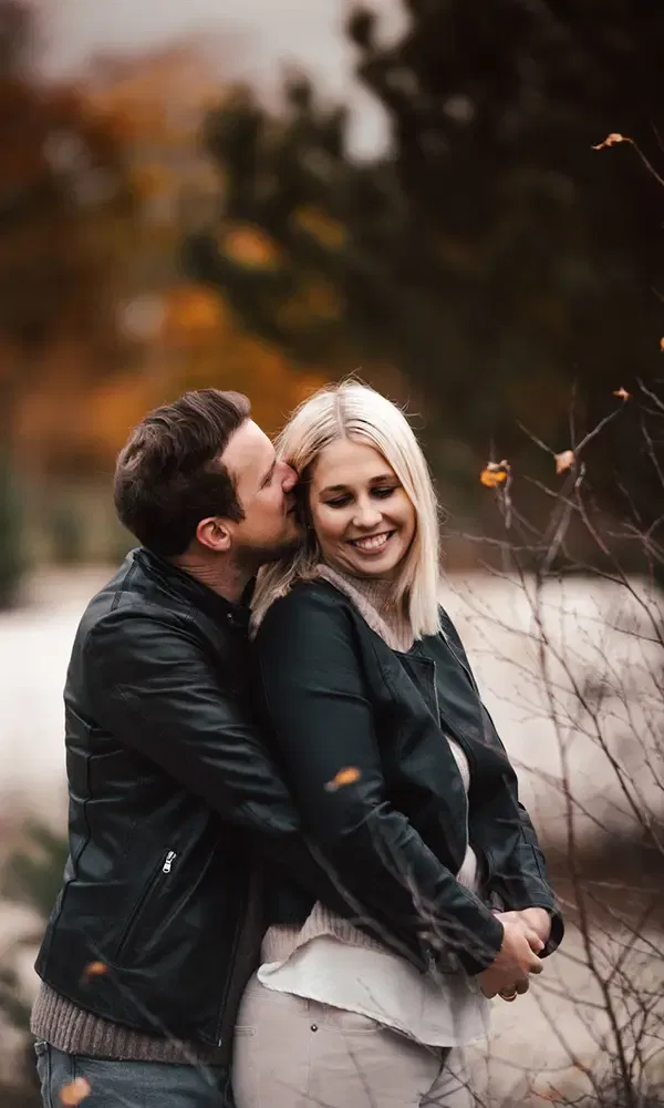 Mann gibt seiner Partnerin einen zärtlichen Kuss auf die Wange, während sie lächelnd die Augen schließt und den Moment genießt.