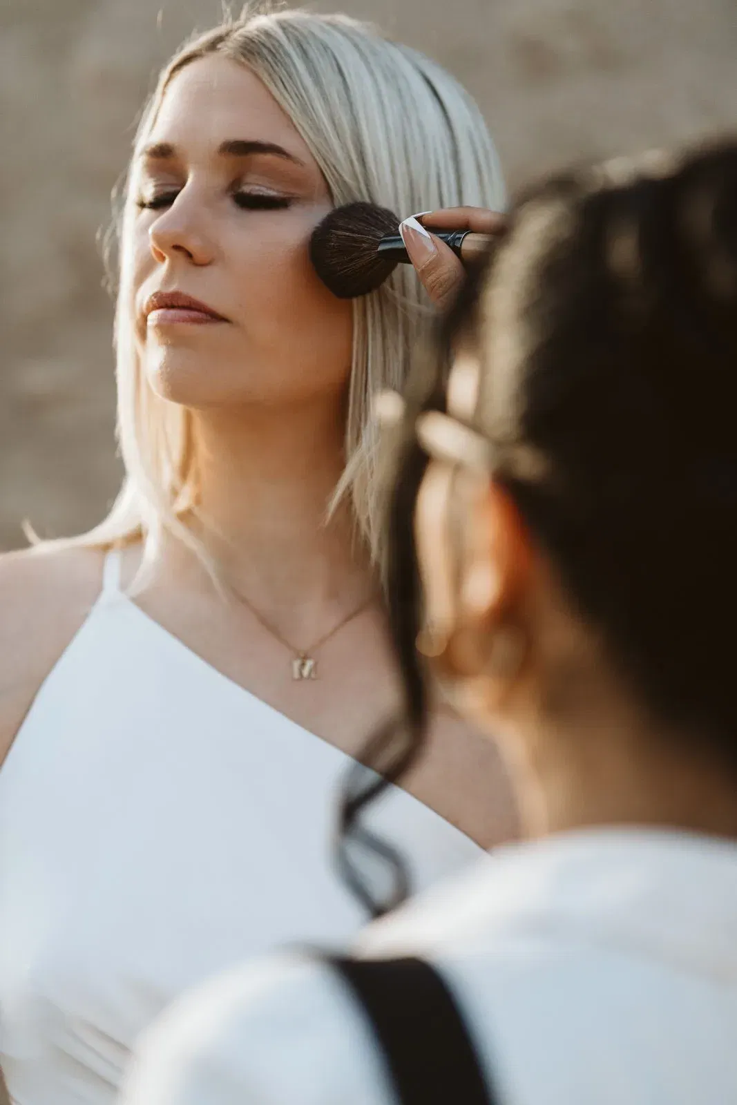 Braut beim Auftragen von Make-up durch eine Visagistin, die einen Pinsel sanft über ihre Wange führt.