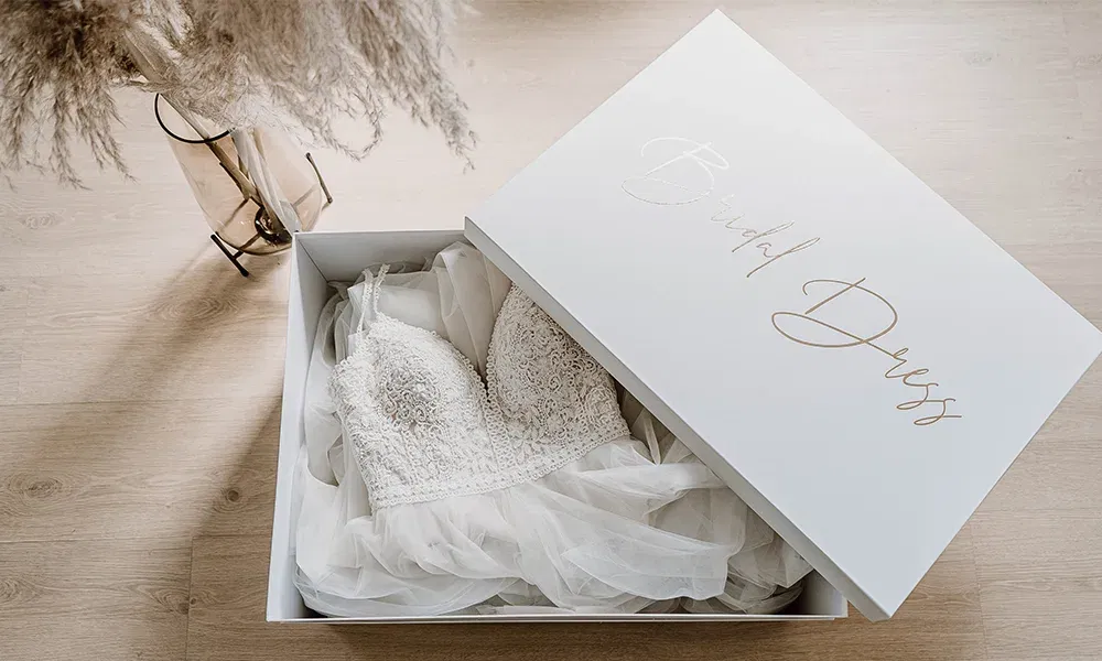 Eine weiße Box in der sich ein verziertes Brautkleid mit Herzausschnitt befindet.