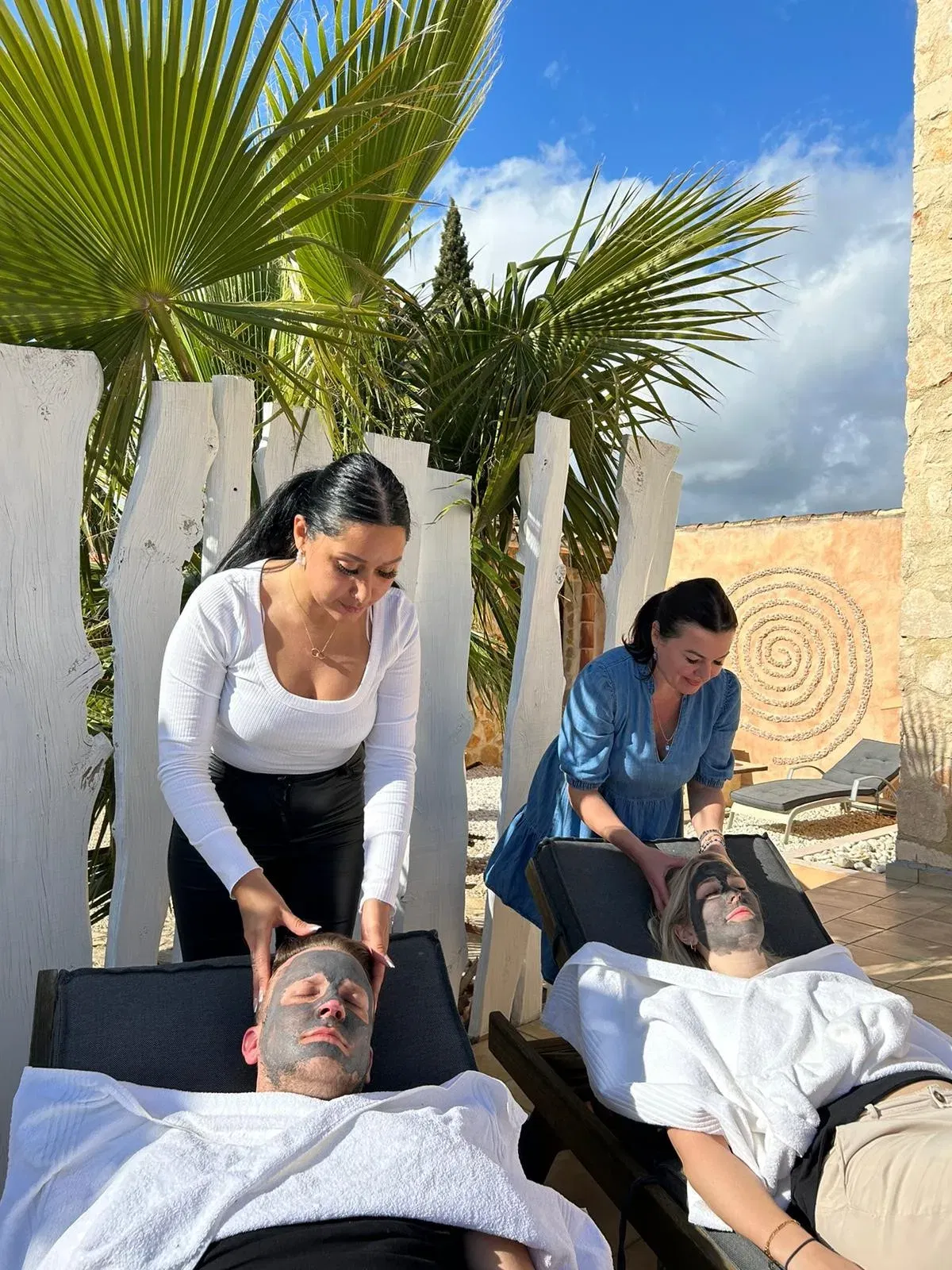 Zwei Personen genießen eine entspannende Gesichtsmaske unter Palmen, während sie eine wohltuende Kopfmassage erhalten.