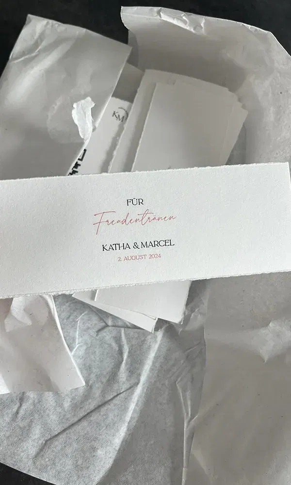 Nahaufnahme einer kleinen Karte mit der Aufschrift „Für Freudentränen“ und den Namen „Katha & Marcel“ sowie dem Hochzeitsdatum „2. August 2024“, als liebevolle Geste für die Hochzeitsgäste.