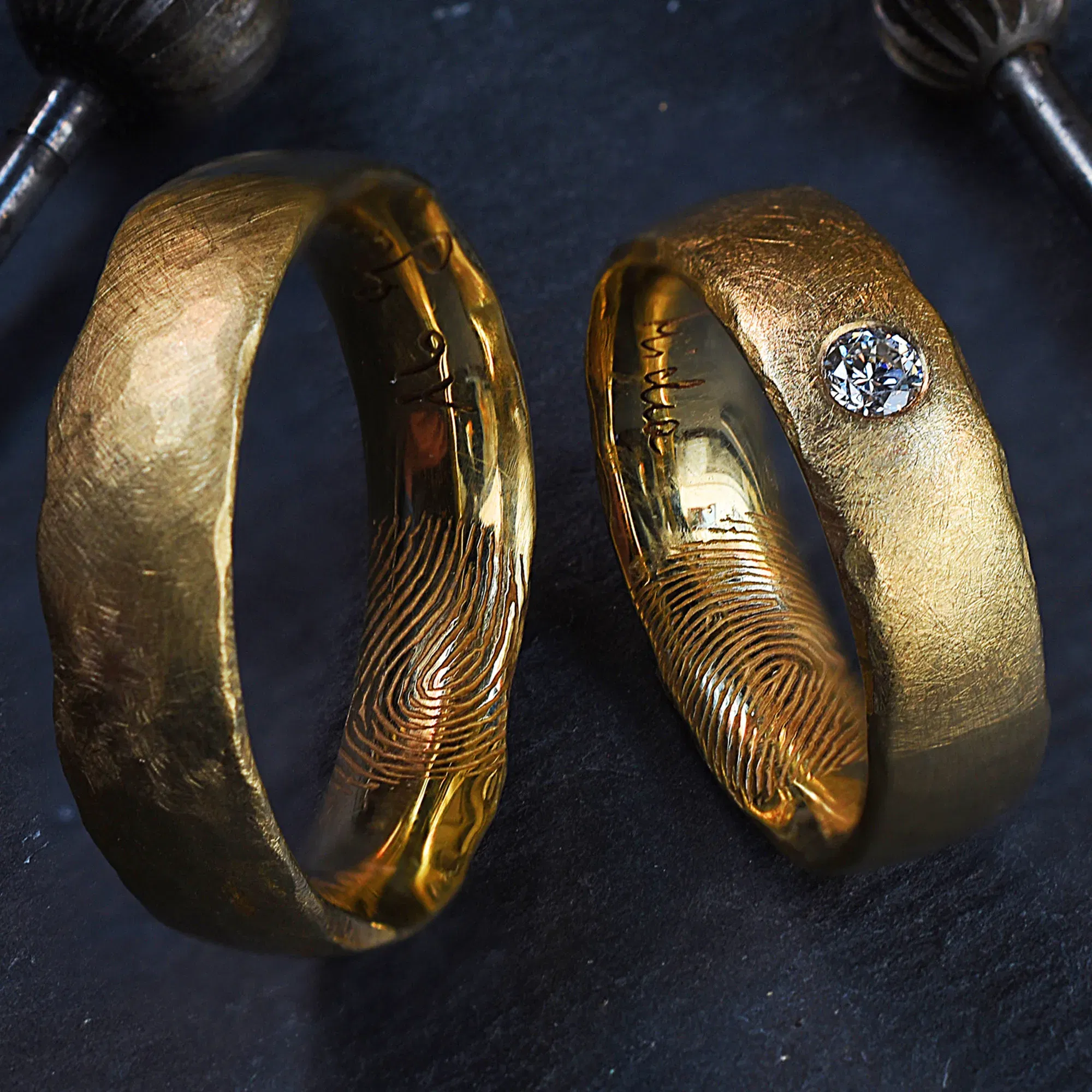 Einzigartige goldene Trauringe, bei denen auf den Innenseiten der Ringe Fingerabdrücke eingraviert sind. Einer der Ringe ist mit einem Diamanten verziert.