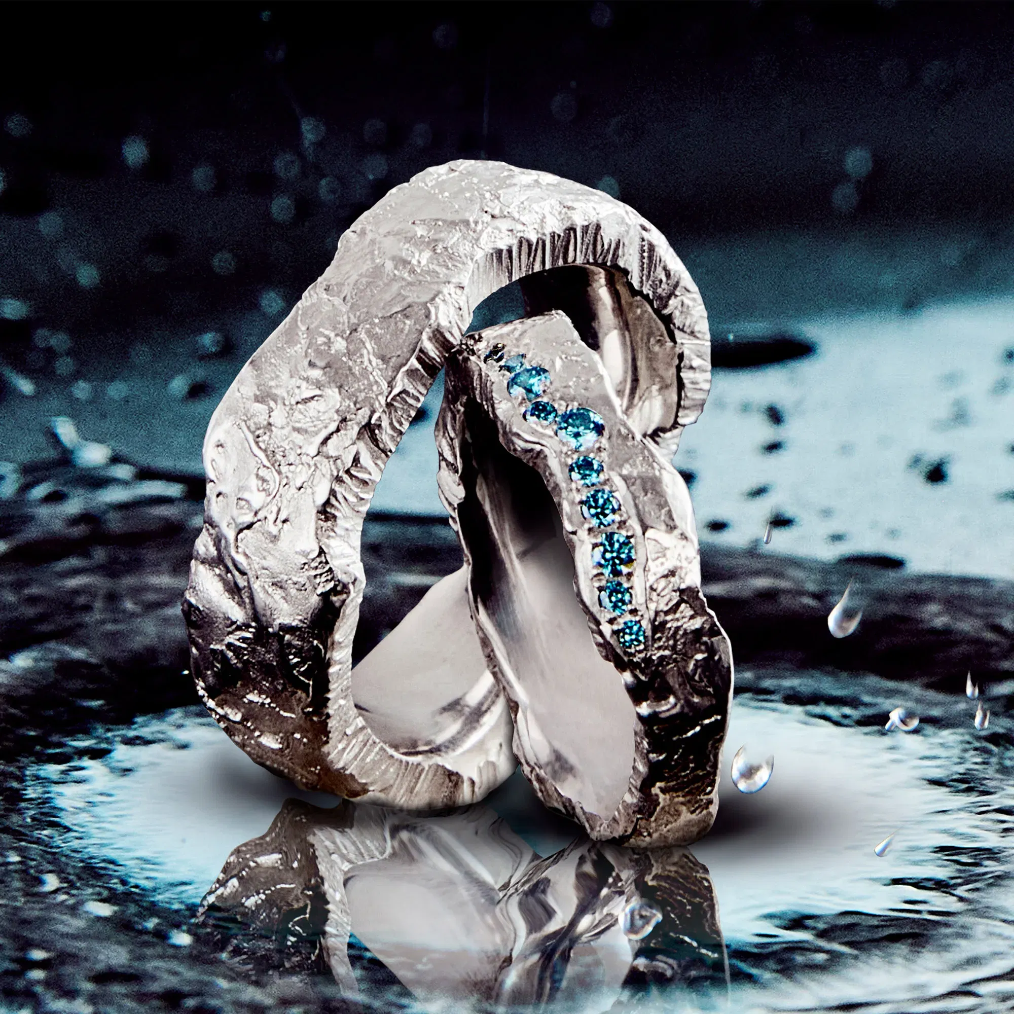 Zwei handgefertigte, rustikale Silberringe mit unregelmäßiger Oberfläche, einer davon mit blauen Edelsteinen besetzt, auf einer Wasseroberfläche fotografiert.
