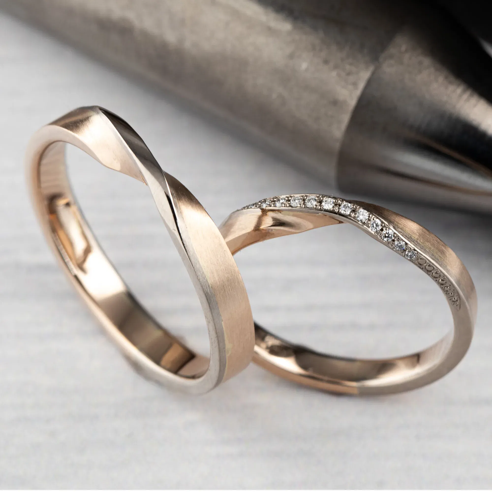 Elegante, minimalistische Eheringe aus Roségold, einer davon mit kleinen Diamanten besetzt, mit einer sanften, geschwungenen Form.