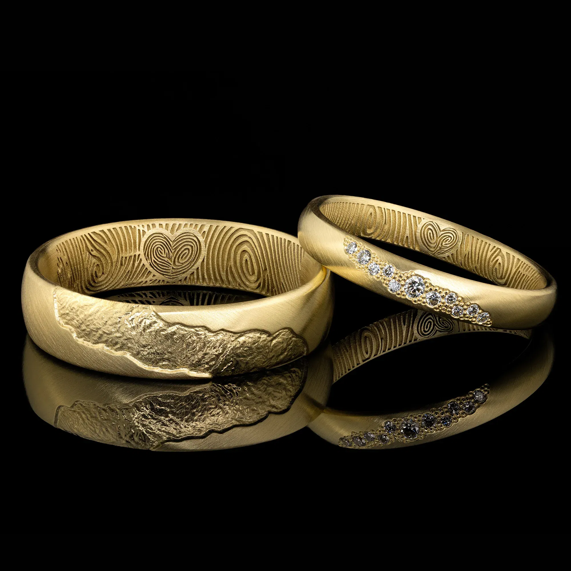 Goldene Trauringe mit handgravierten Details auf der Innenseite, einer mit einem Herz und Fingerabdruck, der andere mit kleinen Diamanten besetzt.