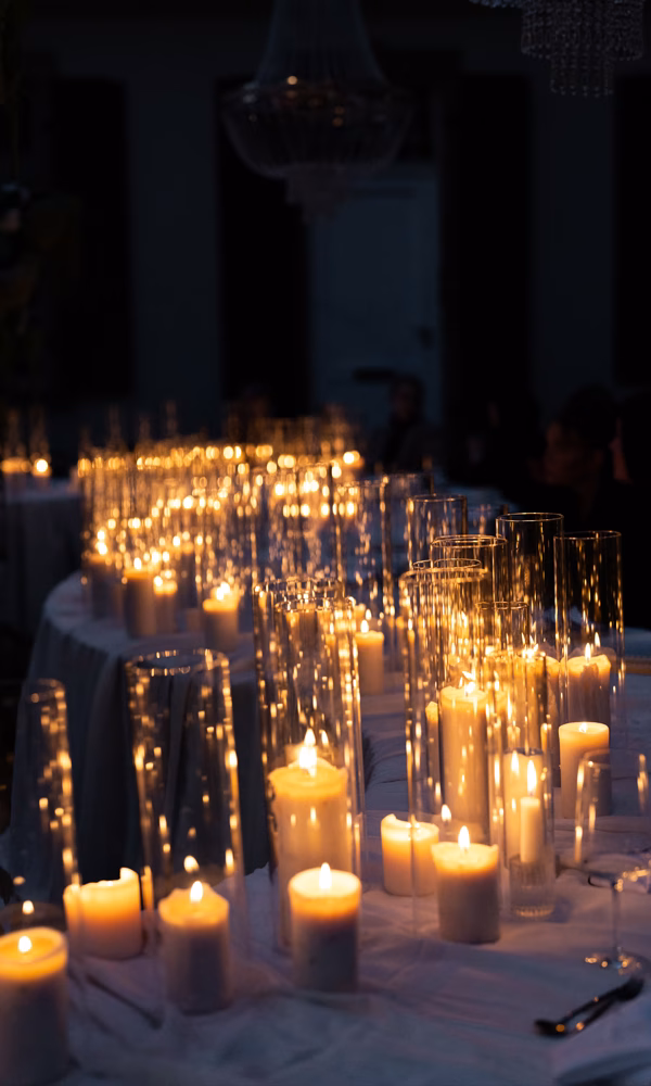 Stimmungsvolle Hochzeitsdeko mit Kerzen in hohen, schlichten Glasgefäßen. Die sanften Lichtreflexe schaffen eine romantische und intime Stimmung bei Nacht.