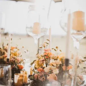 Nahaufnahme eines Hochzeitstisches mit Kerzen und einem prächtigen Blumenarrangement. Die sanfte Abendsonne lässt das gesamte Setting warm und einladend erscheinen.