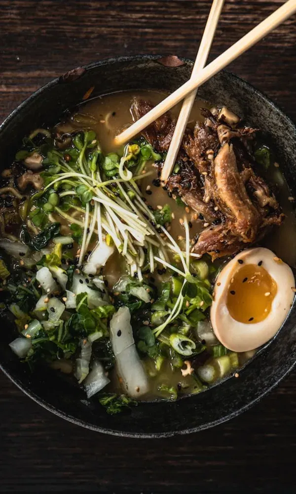Japanische Nudelsuppe mit langsam gegartem Fleisch, einem Soja-Ei, frischem Grün und knackigen Sprossen in dunkler Brühe.