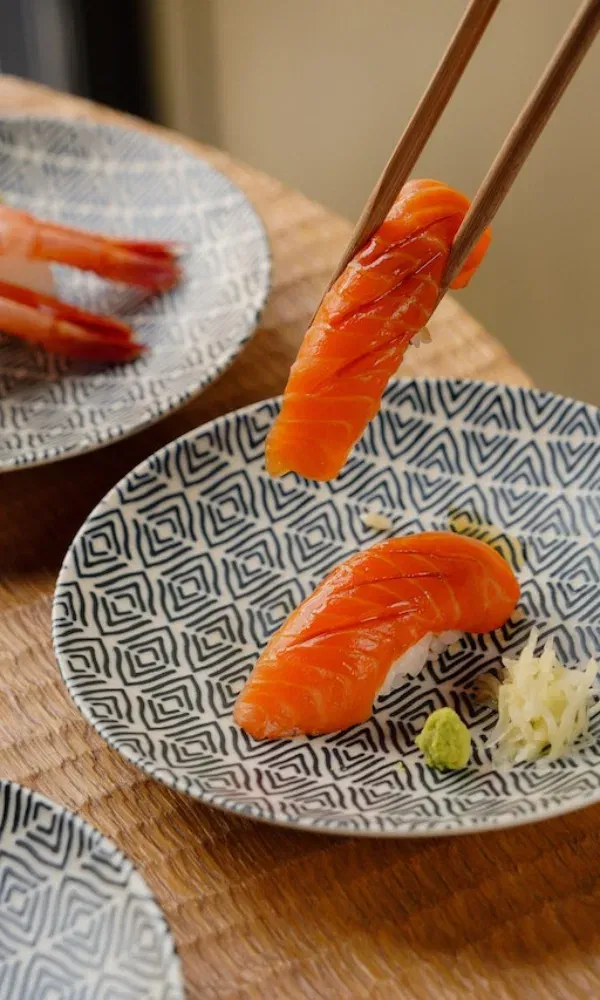 Nahaufnahme von frischem Lachs-Sushi, angerichtet auf einem geometrisch gemusterten Teller, mit Wasabi und Ingwer als Beilage.