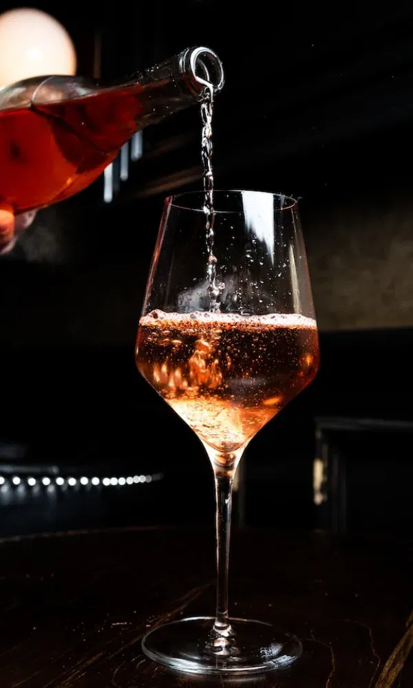 Roséwein wird elegant aus einer Flasche in ein Weinglas gegossen, Bläschen steigen auf, stimmungsvoll beleuchtet.