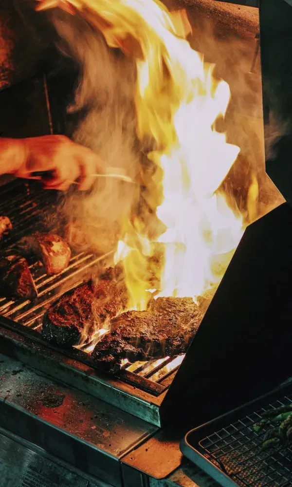 Ein Grillmeister bereitet saftige Fleischstücke über offener Flamme zu – intensives Feuer trifft auf würziges Barbecue.