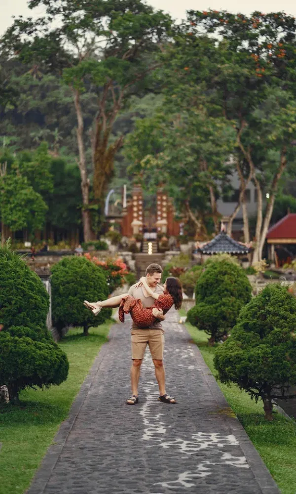 Glückliches Paar im Sommeroutfit, der Mann hält die Frau in den Armen, umgeben von exotischer Gartenarchitektur.