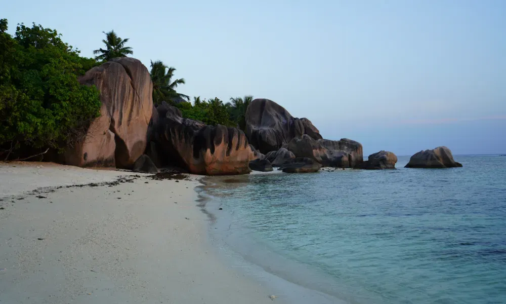 Abendliche Szene an einem tropischen Strand mit auffälligen Felsformationen und ruhiger Meeresoberfläche.