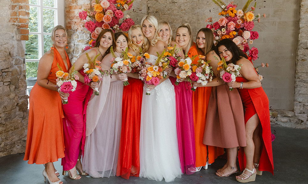 Hochzeitsfoto mit der Braut und ihren Brautjungfern vor einer blumengeschmückten Kulisse.